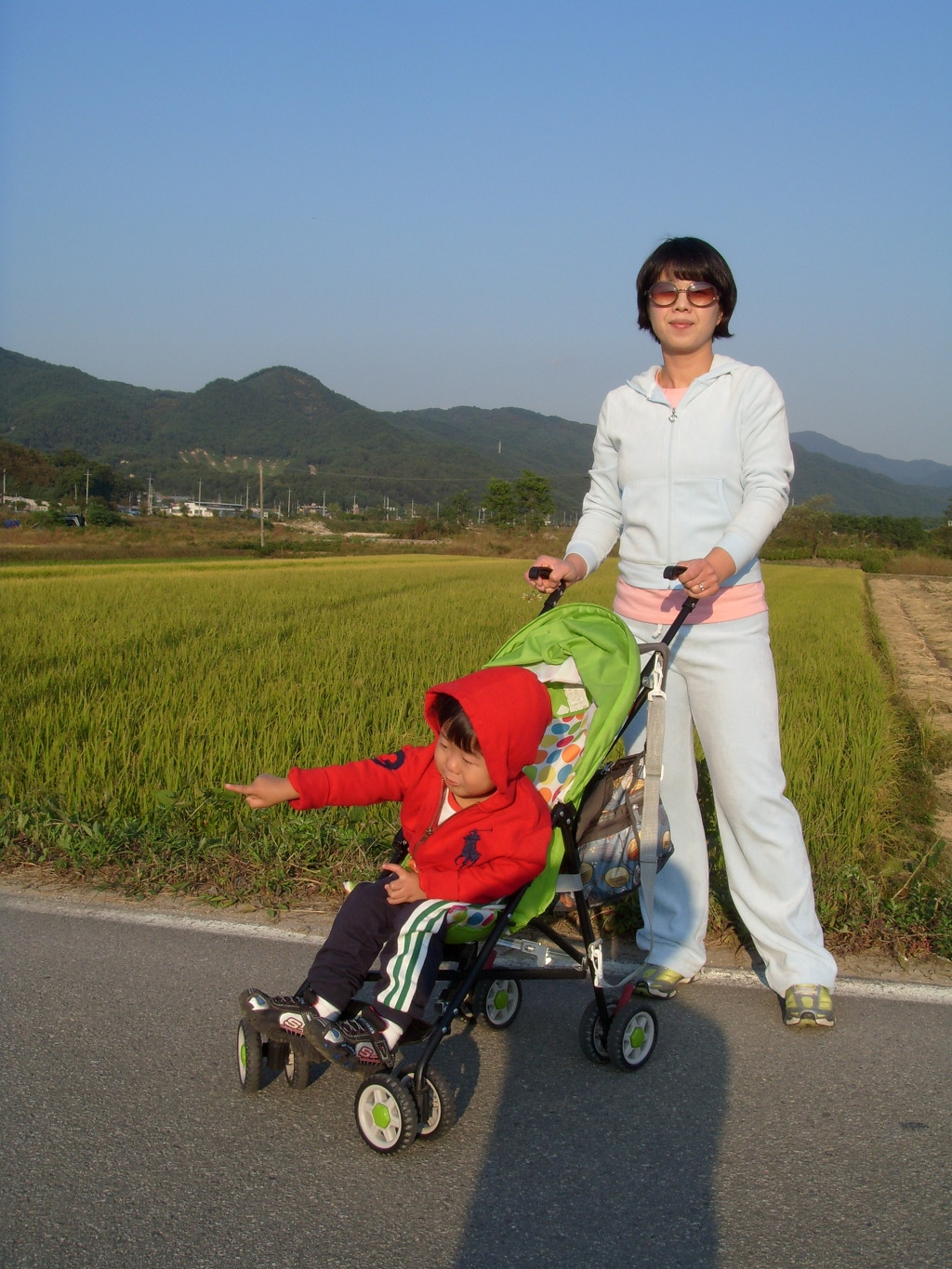 선글라스 성인 유모차 밀고, 빨간 후드 아이 논밭 가리킴