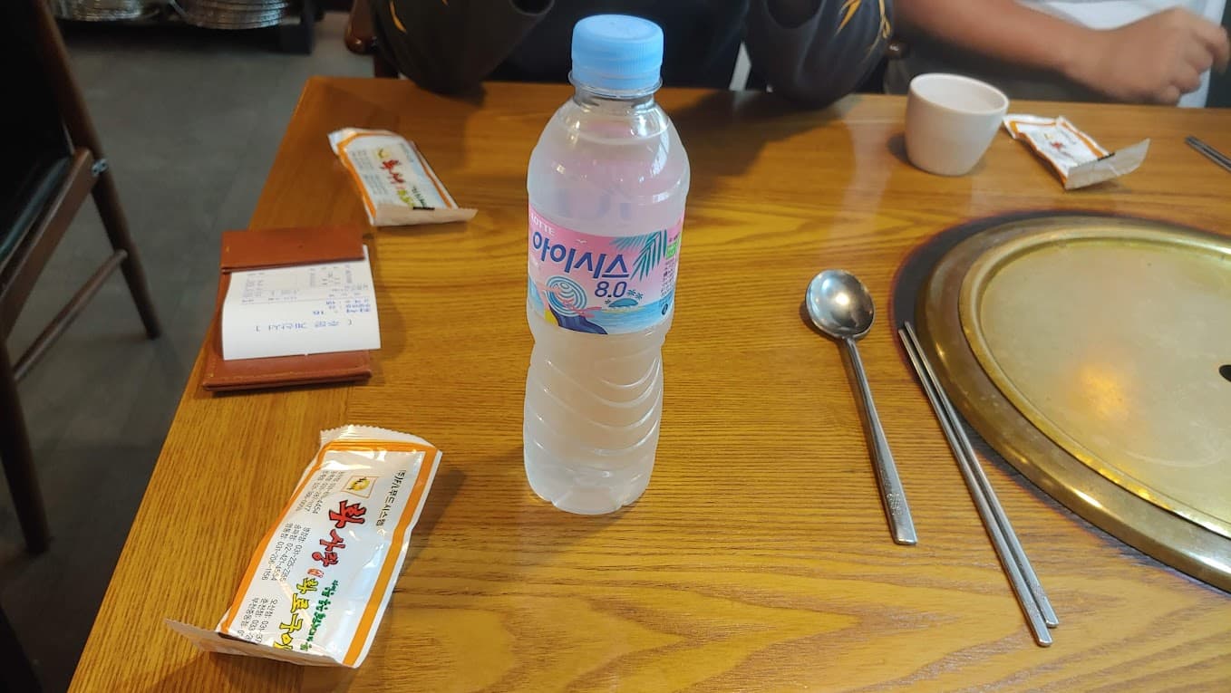 나무 식탁 위 롯데 아이시스 생수병, 식기, 영수증, 불판.