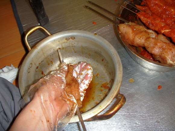 장갑 손으로 생닭 꼬치에 양념 바르기, 다른 닭꼬치 대기 중