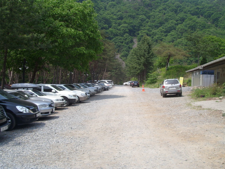 자갈 주차장, 줄지어 선 차량, 울창한 숲, 산악 배경