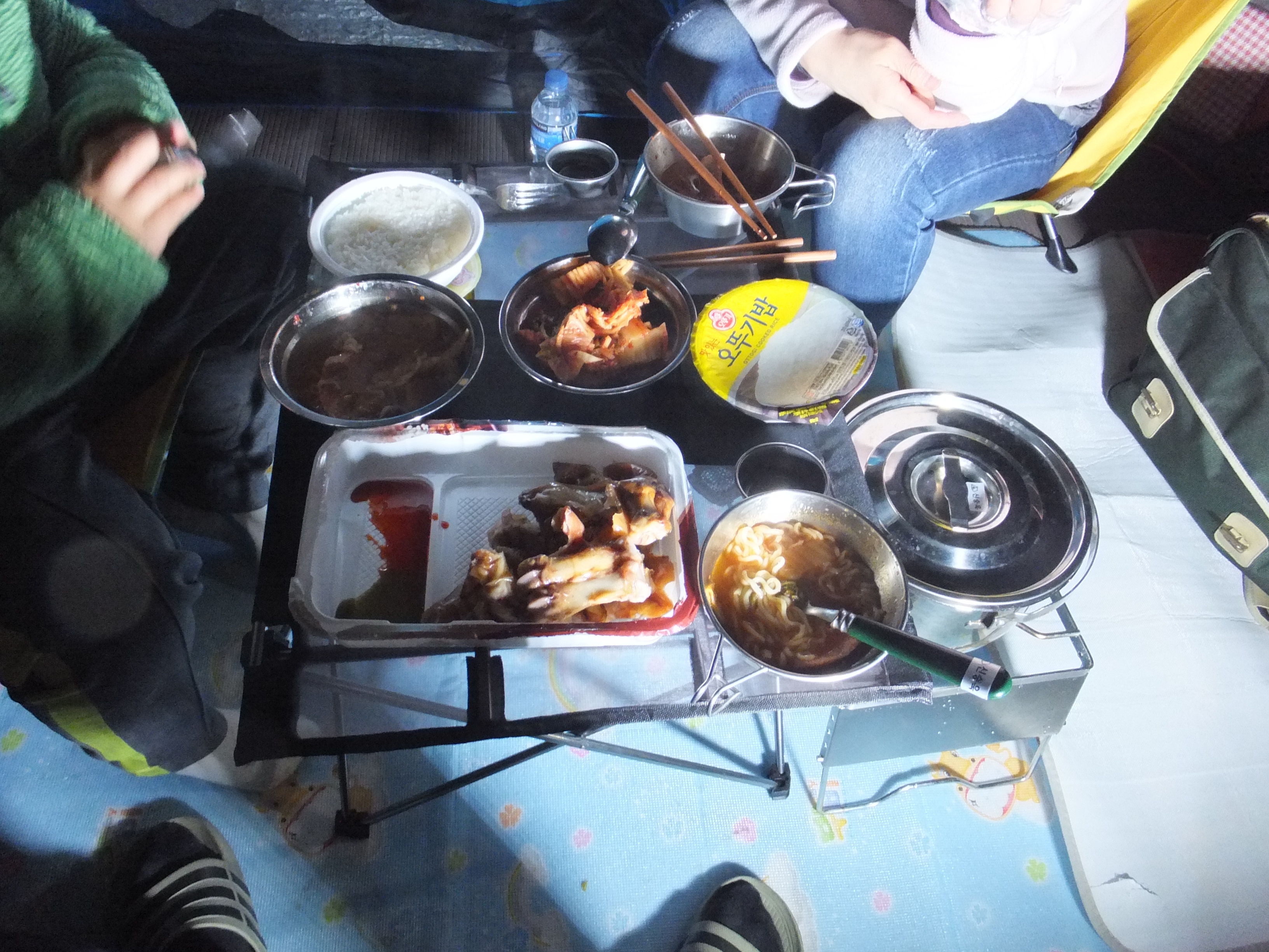 캠핑 테이블 위 밥, 김치, 라면, 닭발, 찌개.