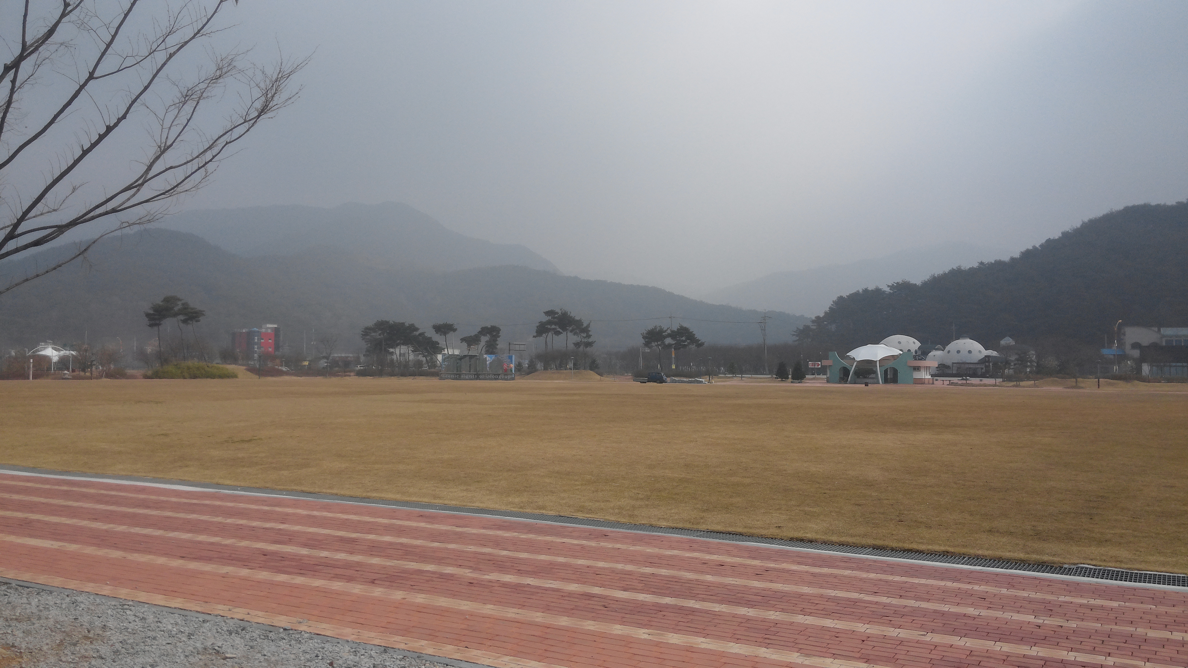 넓은 잔디밭, 붉은 벽돌길, 앙상한 나무, 흐린 산과 돔 건물