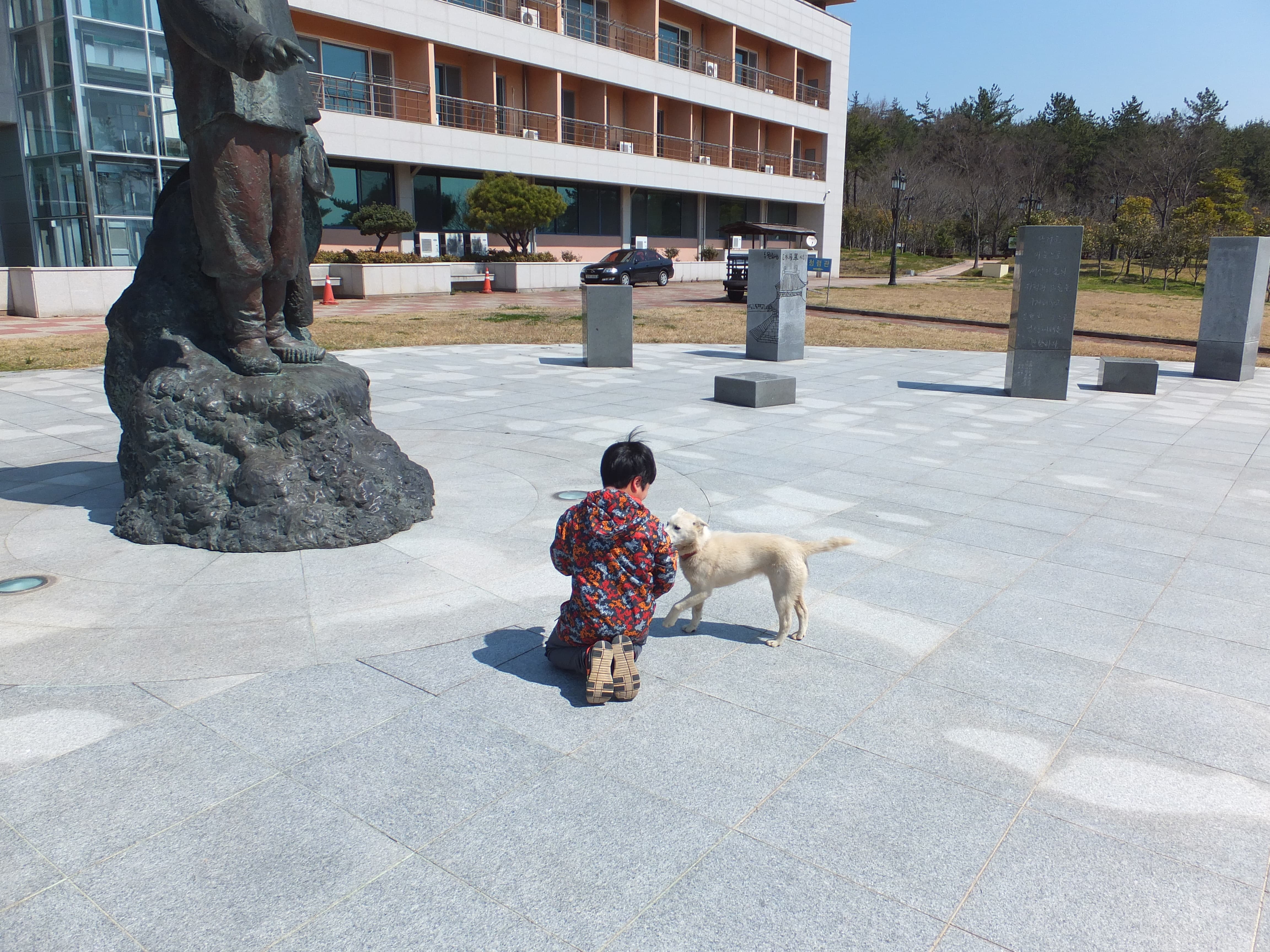 알록달록 옷차림 무릎 꿇고 강아지와 교감, 동상 건물 앞.