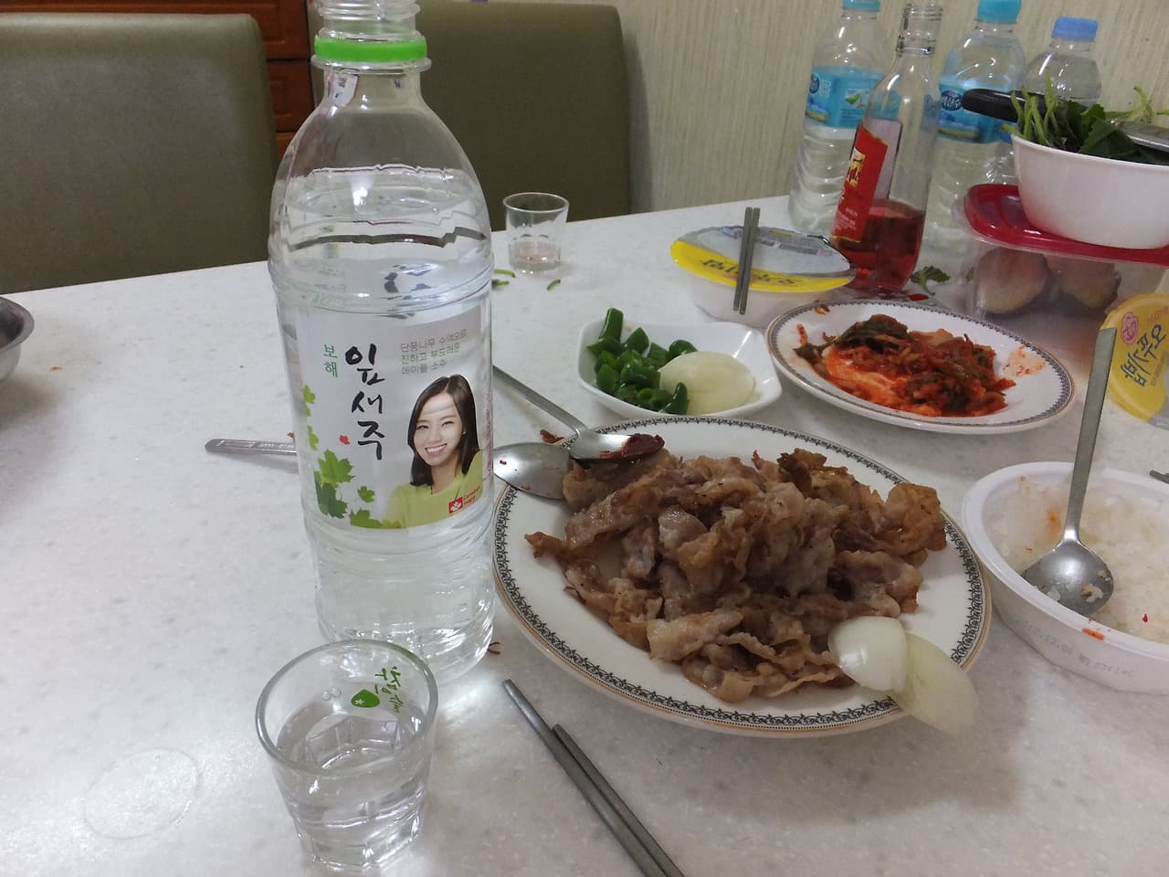 잎새주 병, 푸짐한 구운 돼지고기, 김치, 반찬 식탁