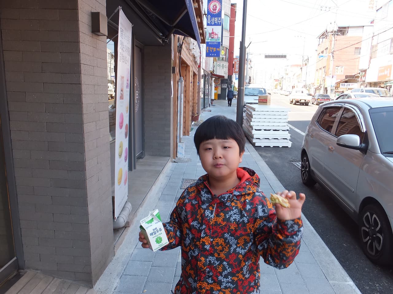 도시 길가 화려한 재킷 어린이 우유팩, 과자 쥐고 서있다.