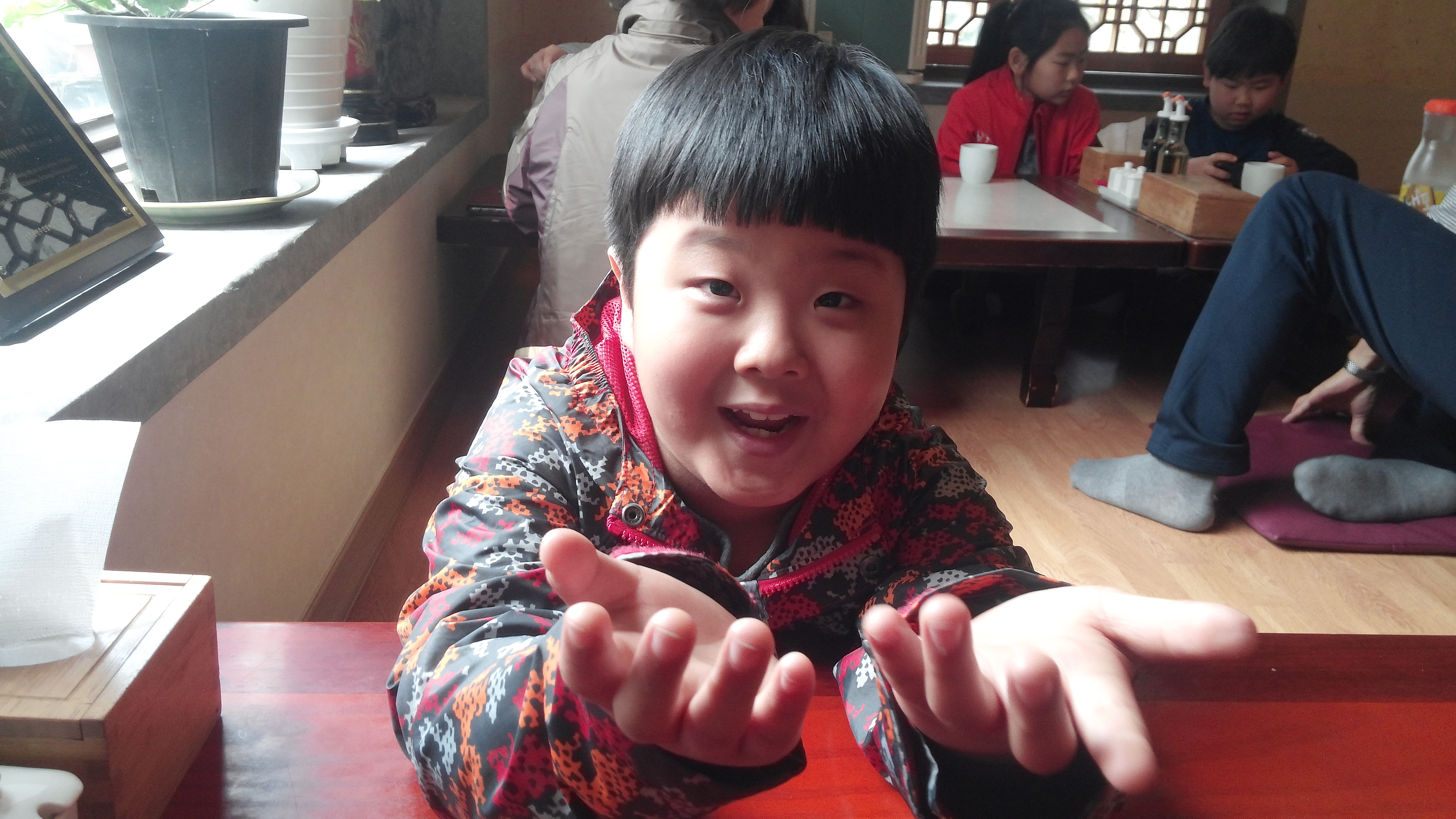 웃는 어린아이, 주황 무늬 재킷 입고 양손 펼쳐 보임