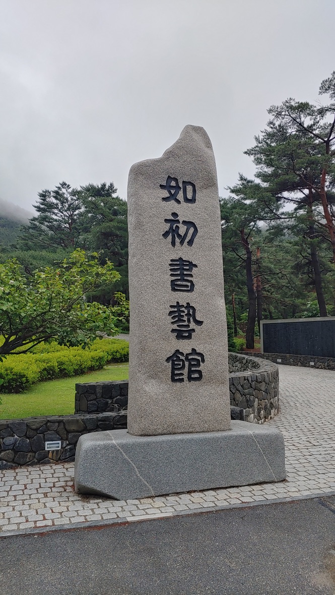회색 화강암 기념비, 여초서예관 한자, 푸른 소나무, 포장 도로