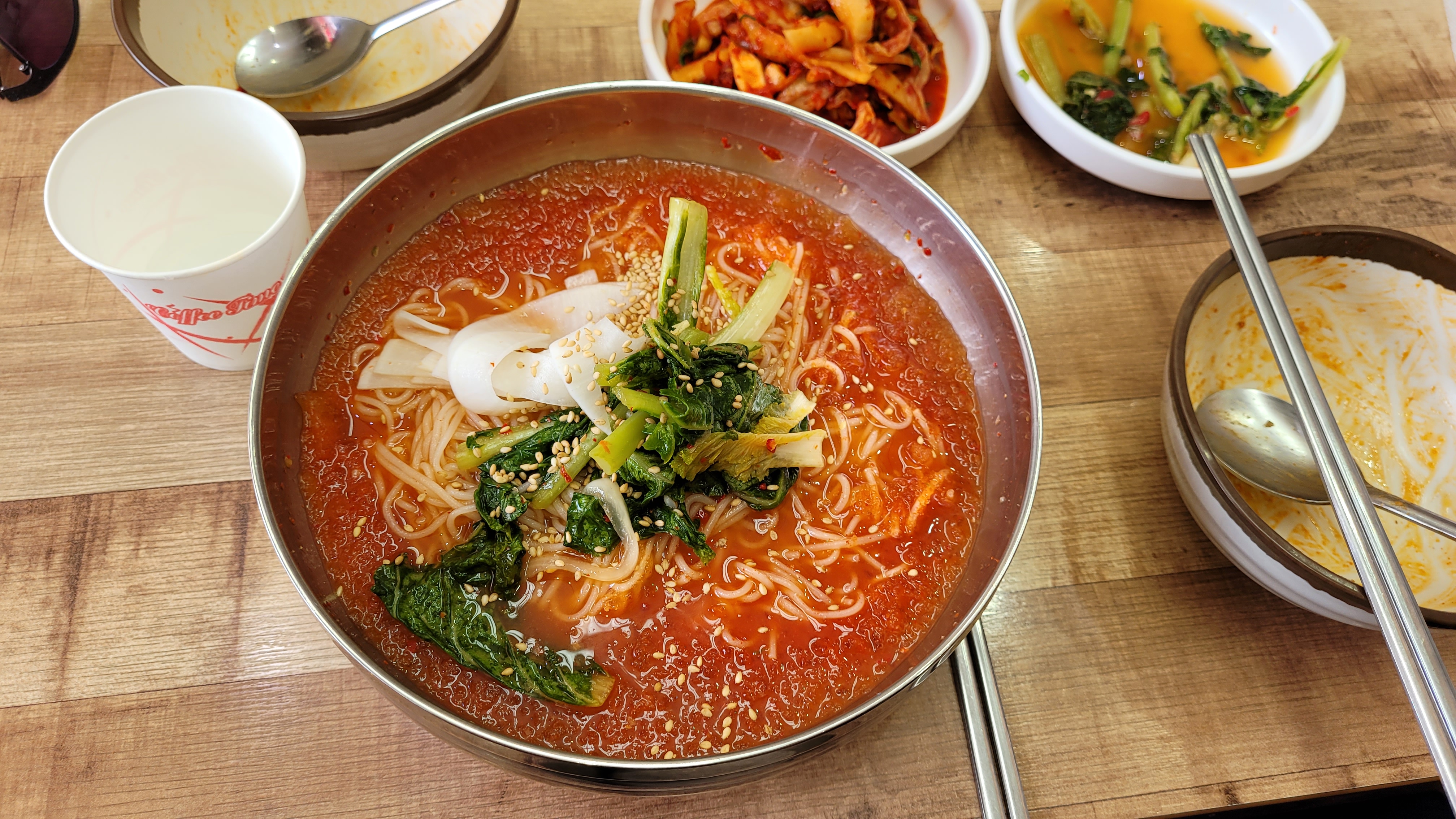 빨간 비빔국수, 푸른 채소와 깨, 다양한 반찬, 나무 식탁