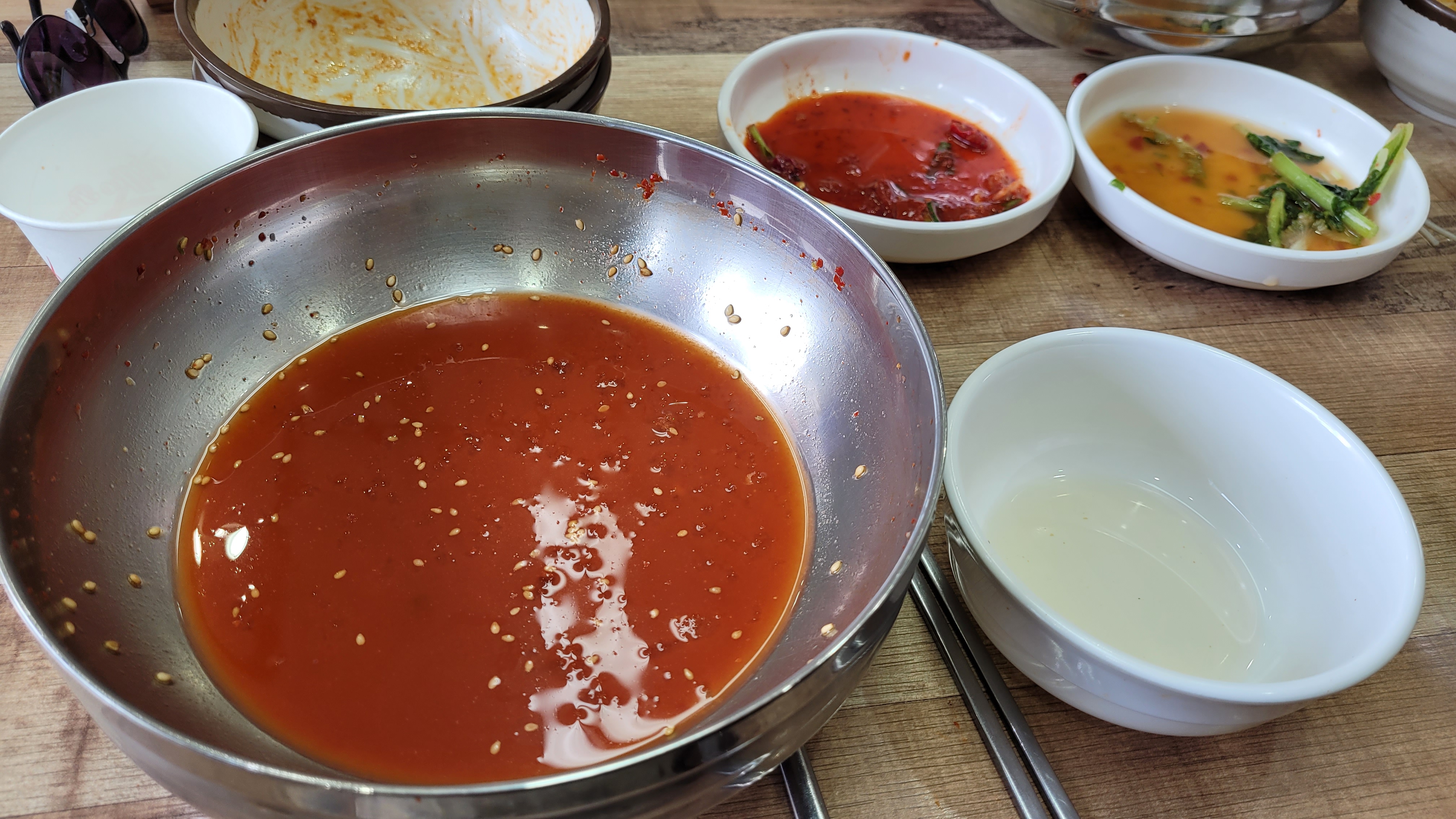 금속 그릇 매콤한 비빔 양념, 참깨와 다양한 한국 반찬들.