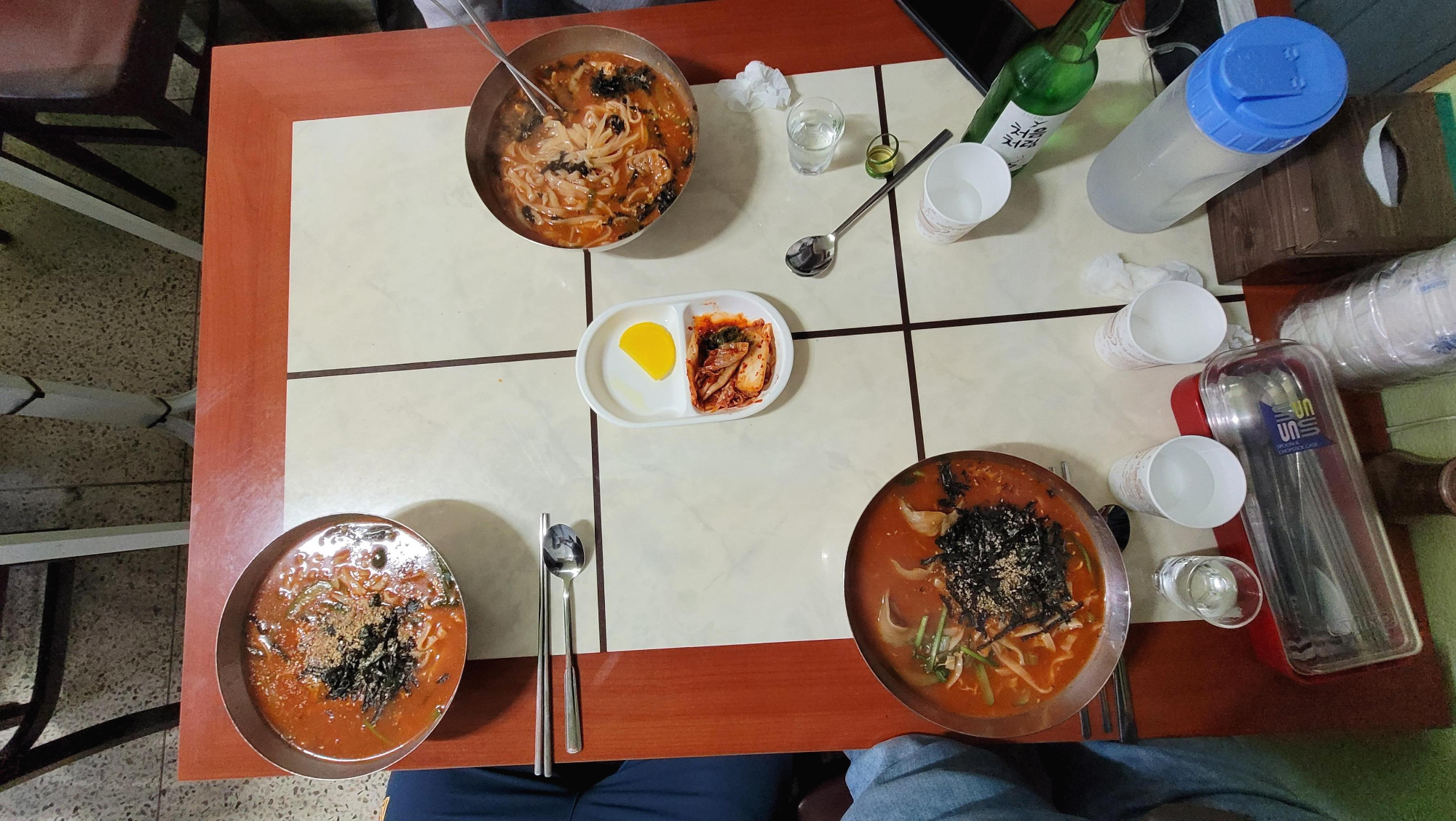매콤한 칼국수 세 그릇, 김치, 단무지, 소주 탁자 위