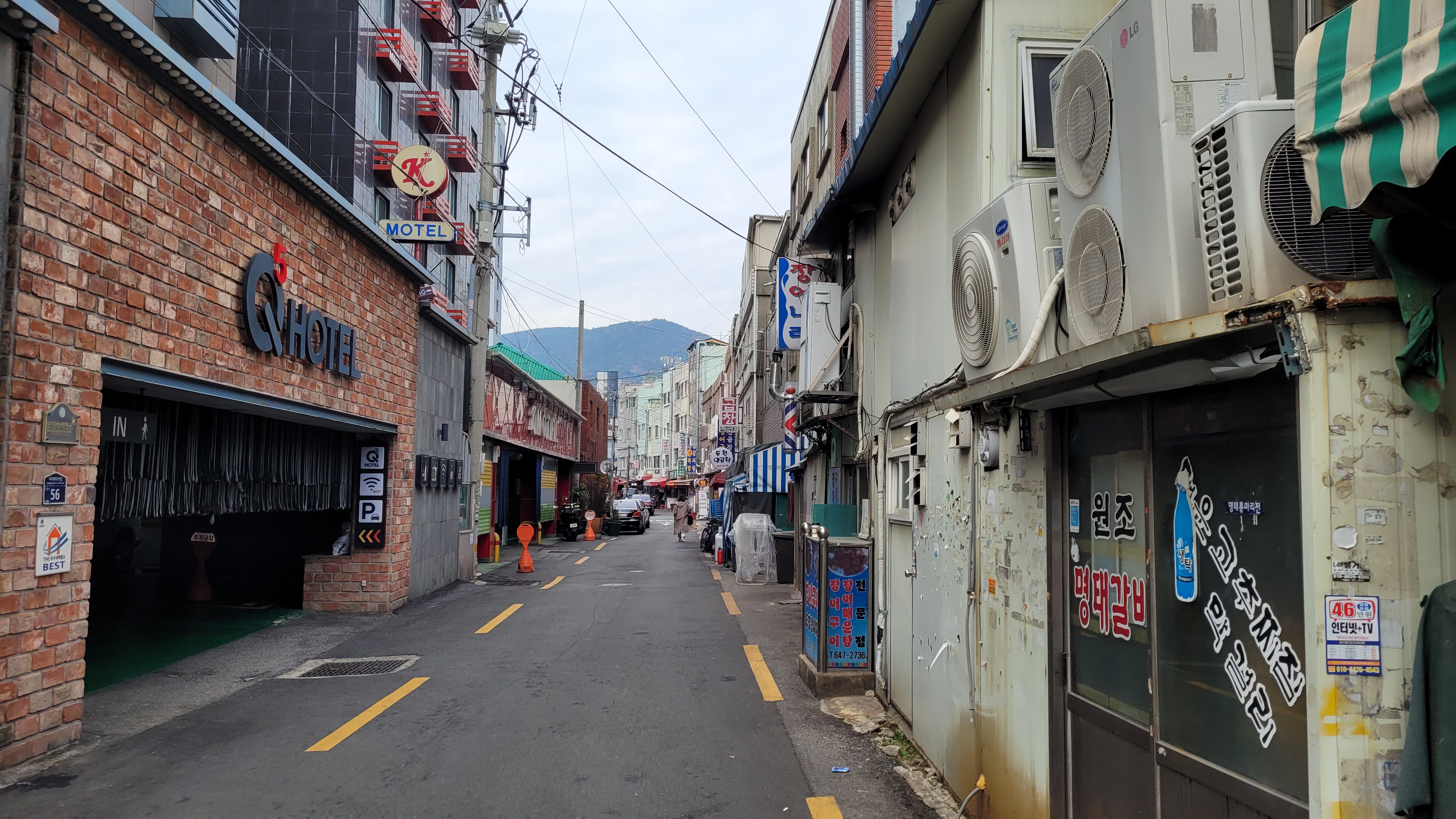 벽돌 Q호텔, K모텔 간판, 낡은 상가, 실외기, 산 배경 골목