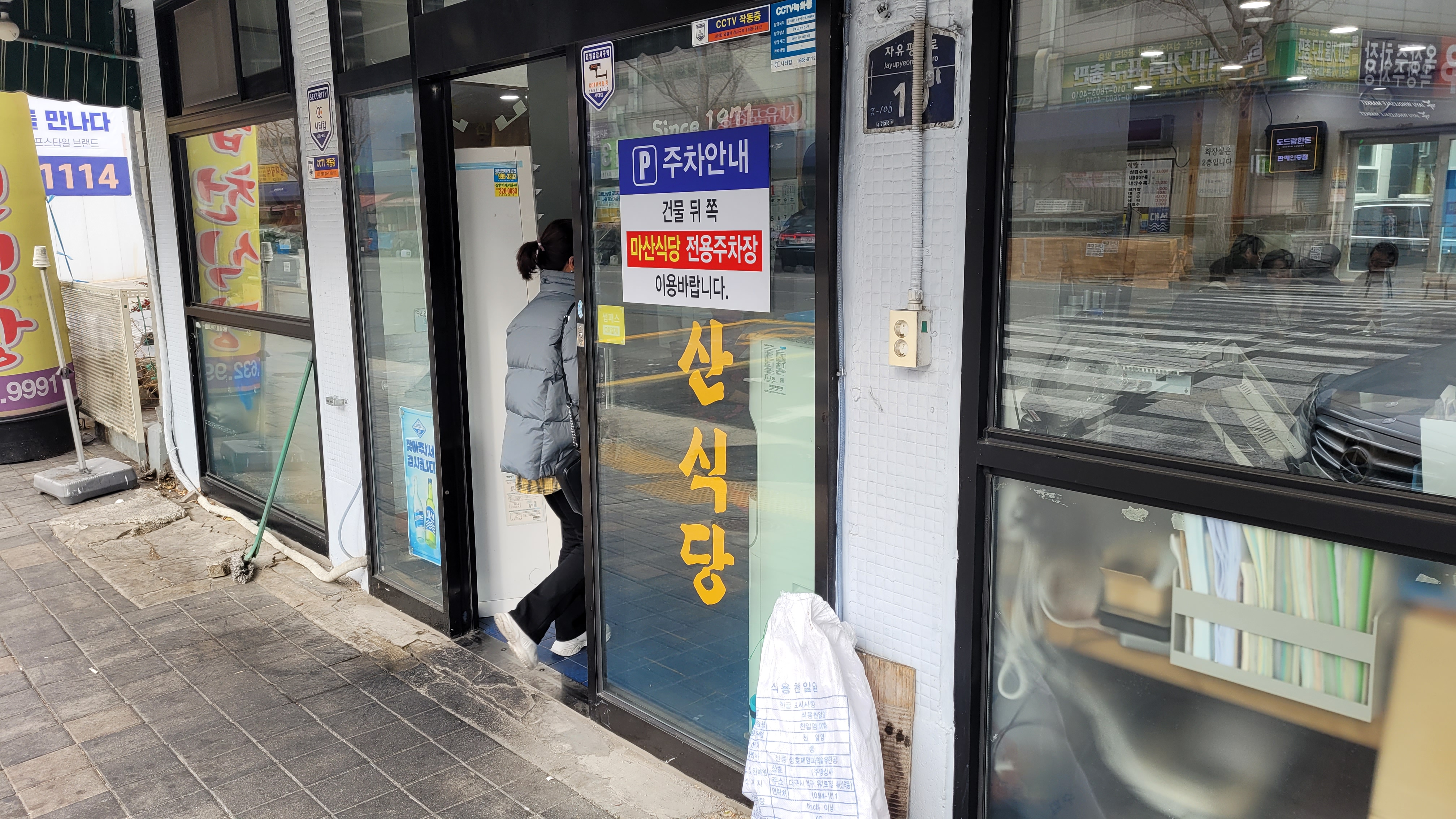 회색 패딩 재킷 출입문 통과, 산식당 간판, 주차 안내문