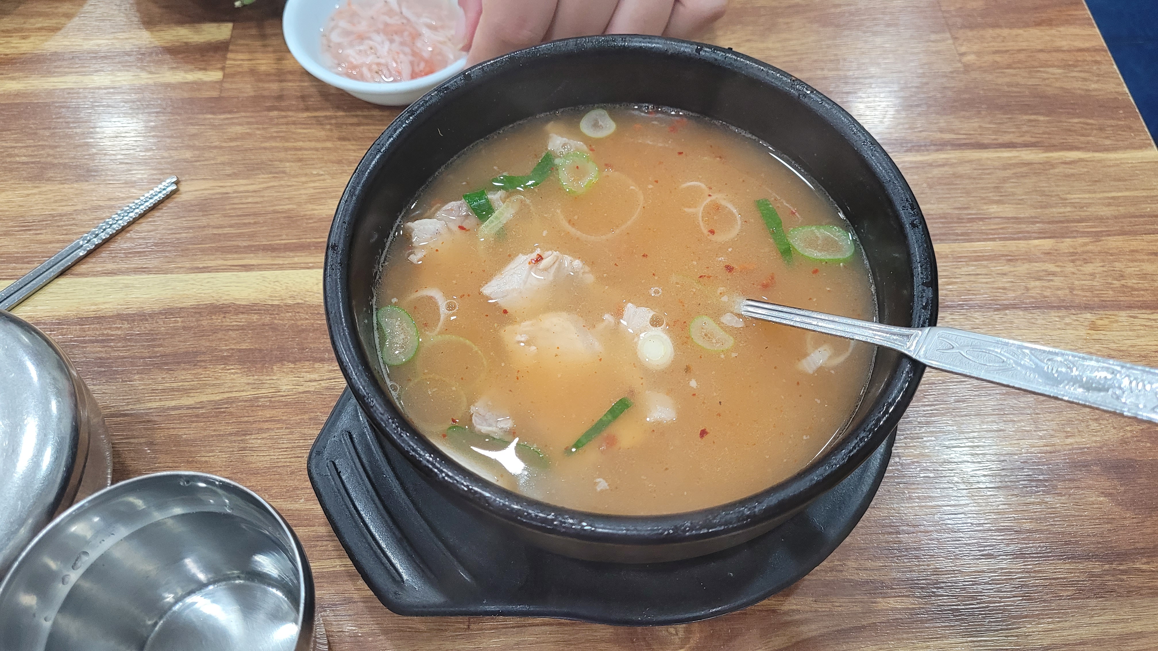 따뜻한 돼지국밥, 뚝배기, 숟가락, 송송 썬 파, 새우젓, 나무