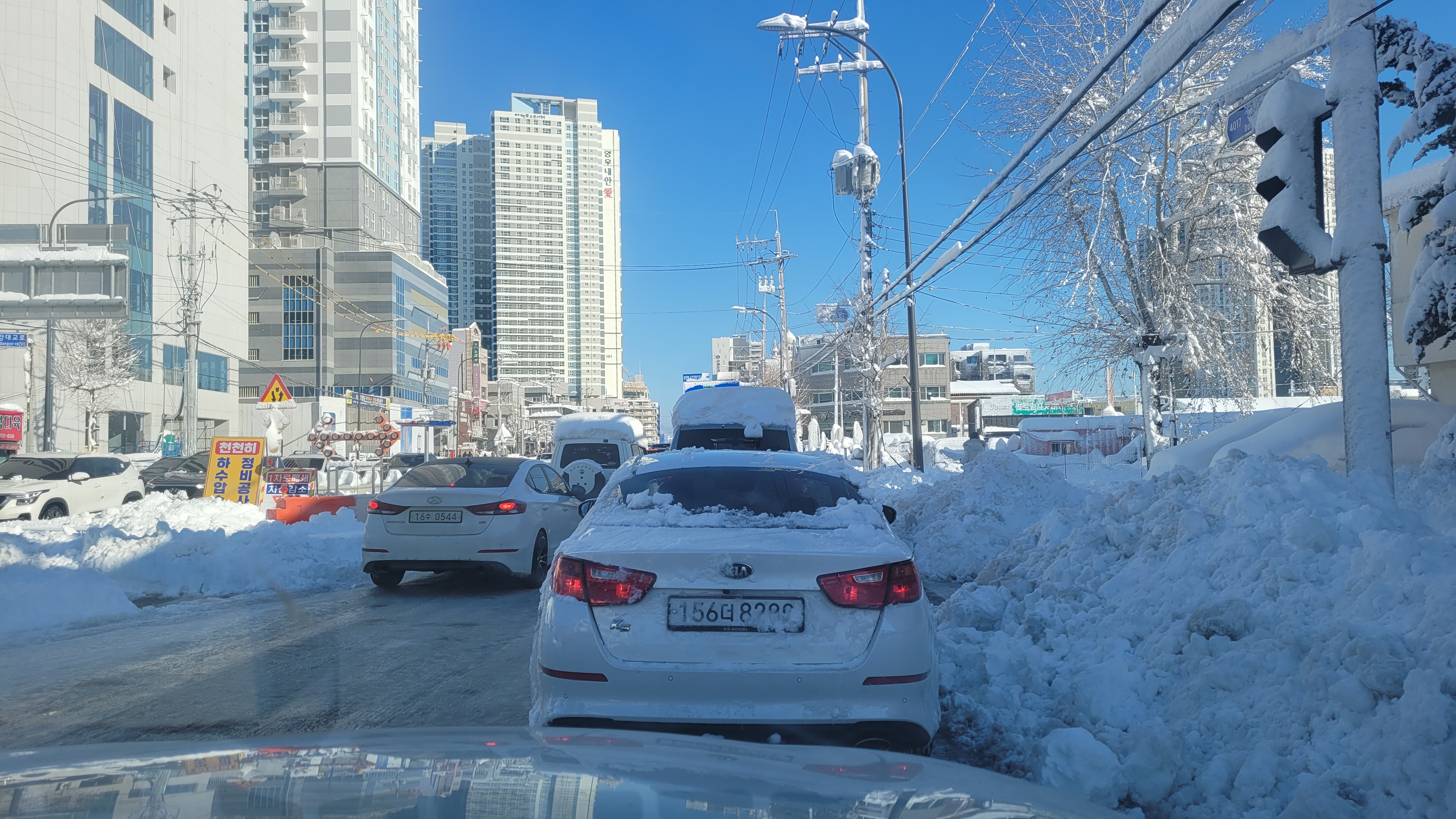 설경 도시 도로, 주차 차량, 고층 아파트 단지, 푸른 하늘