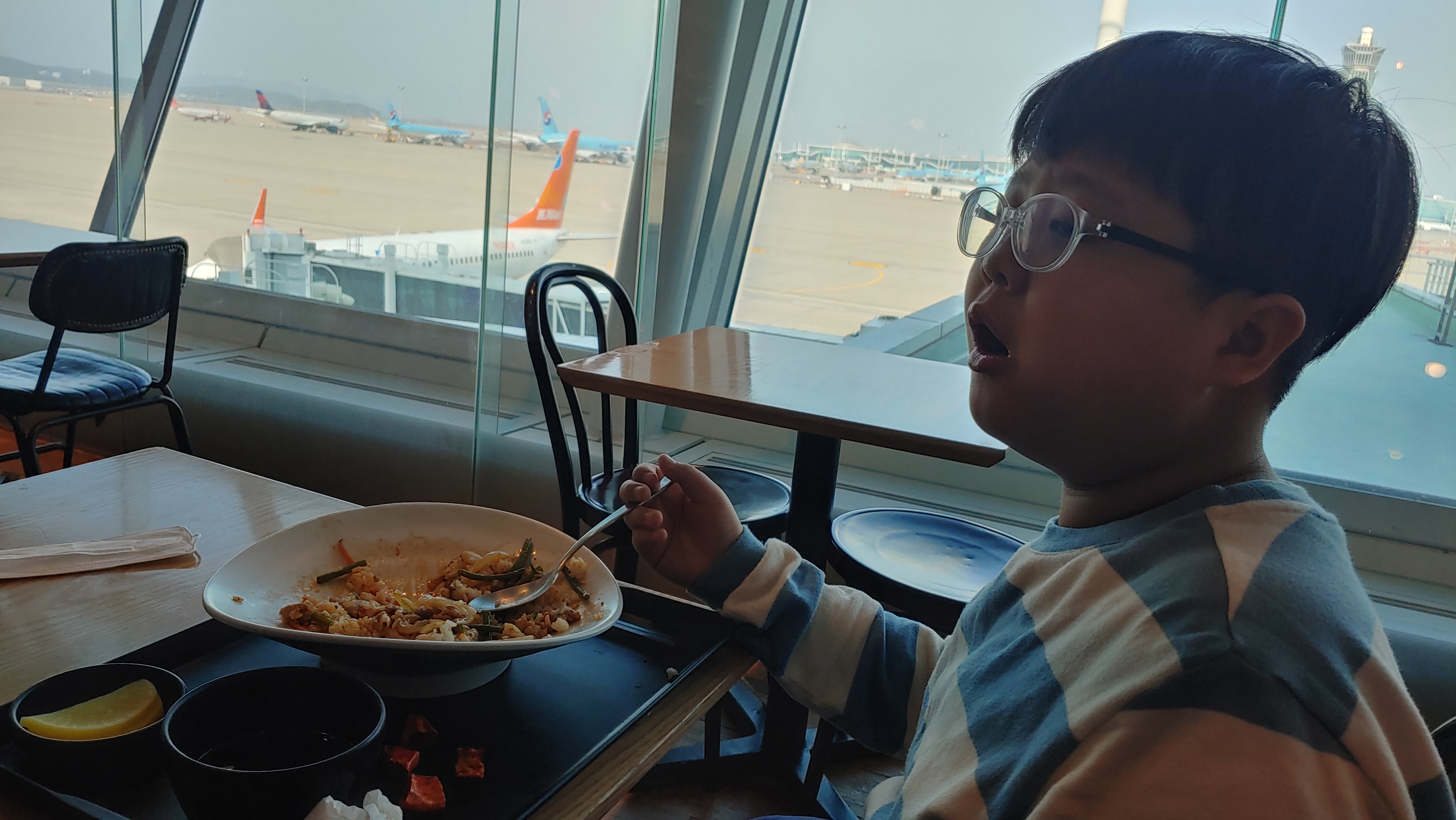 공항 식당에서 안경 쓴 채 비행기 보며 식사 중