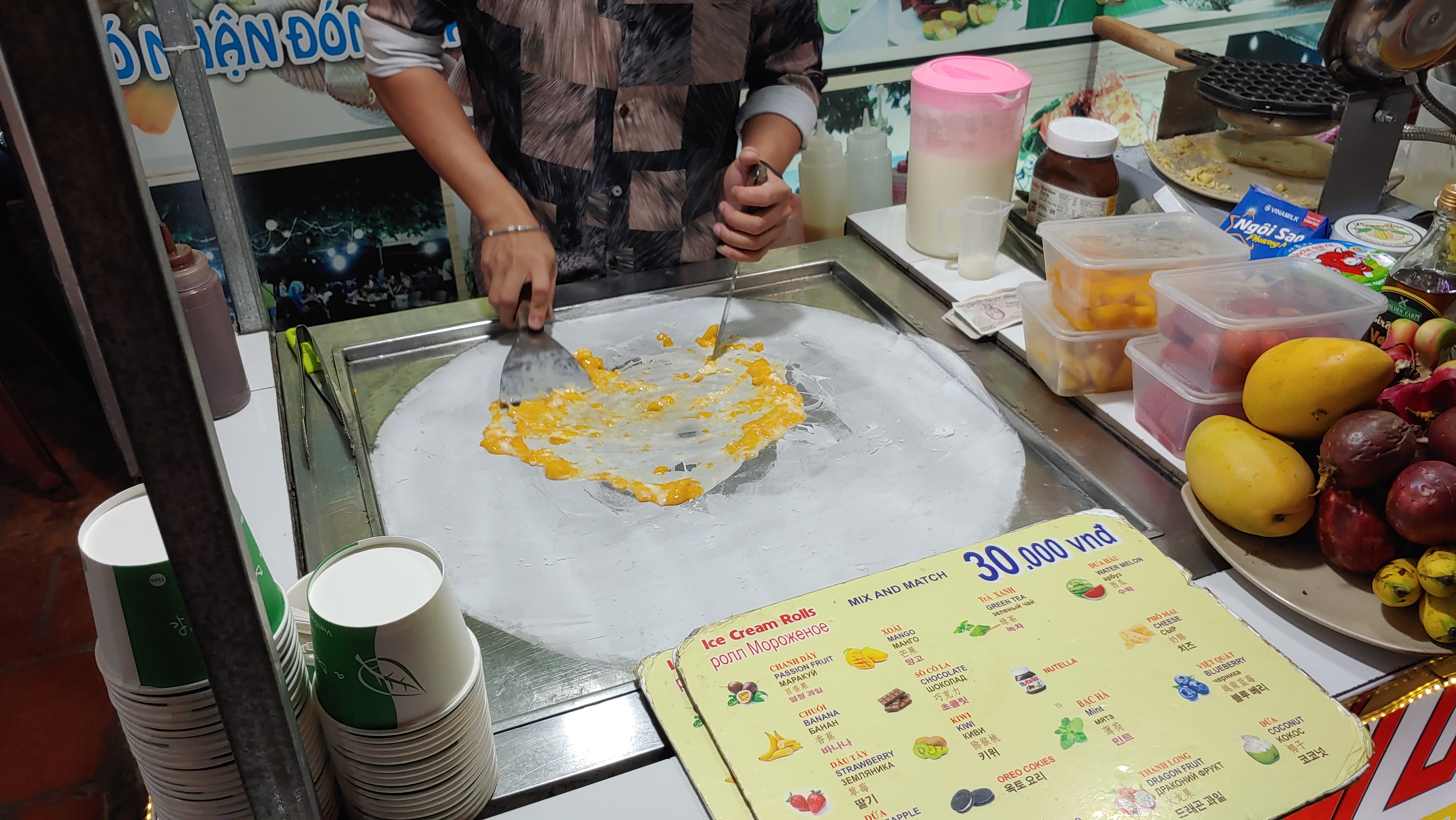 신선한 망고 롤 아이스크림 차가운 철판 위 제조, 다양한 과일 진열.