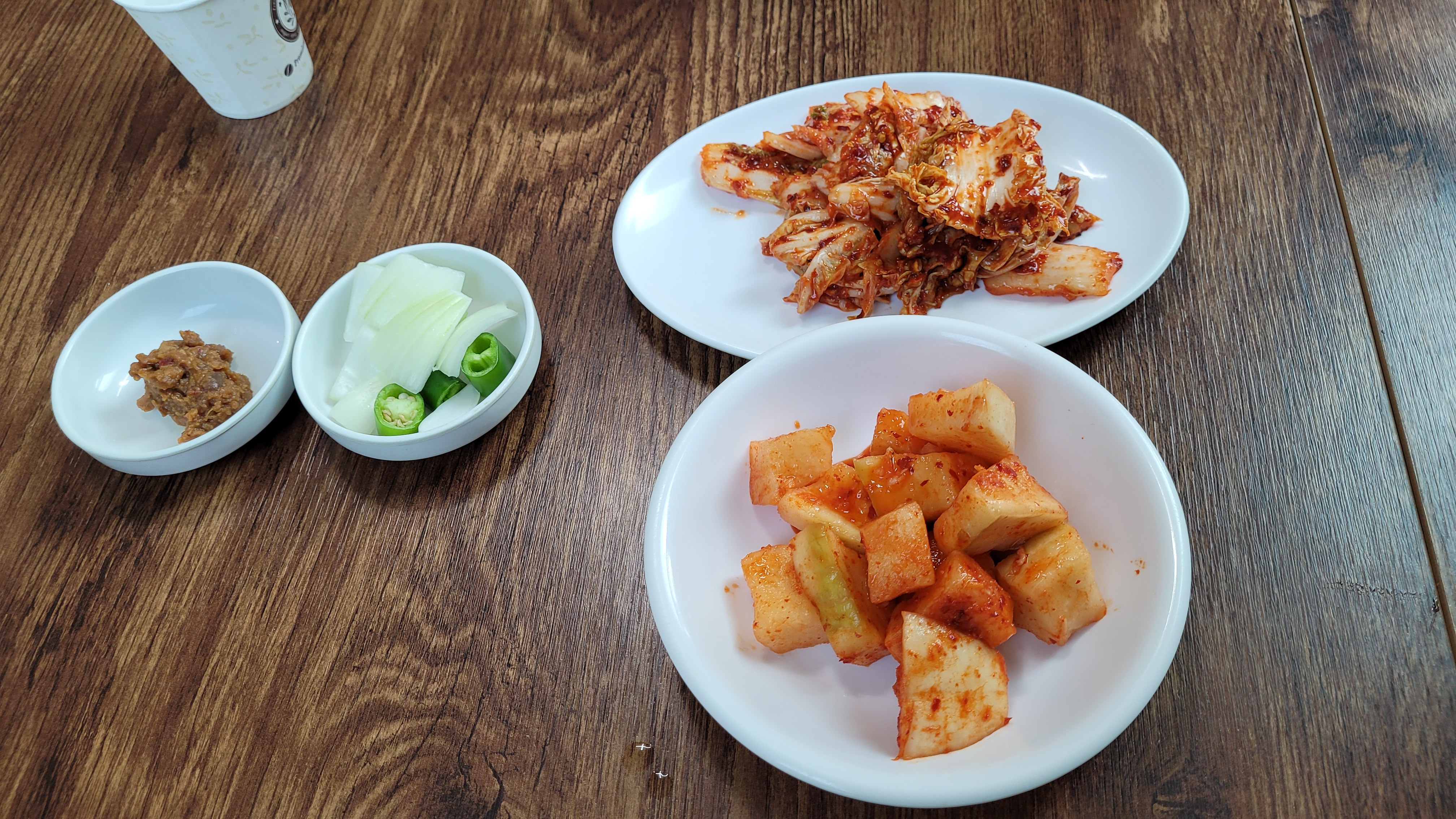 테이블 위 배추김치, 깍두기, 쌈장, 양파, 고추 반찬