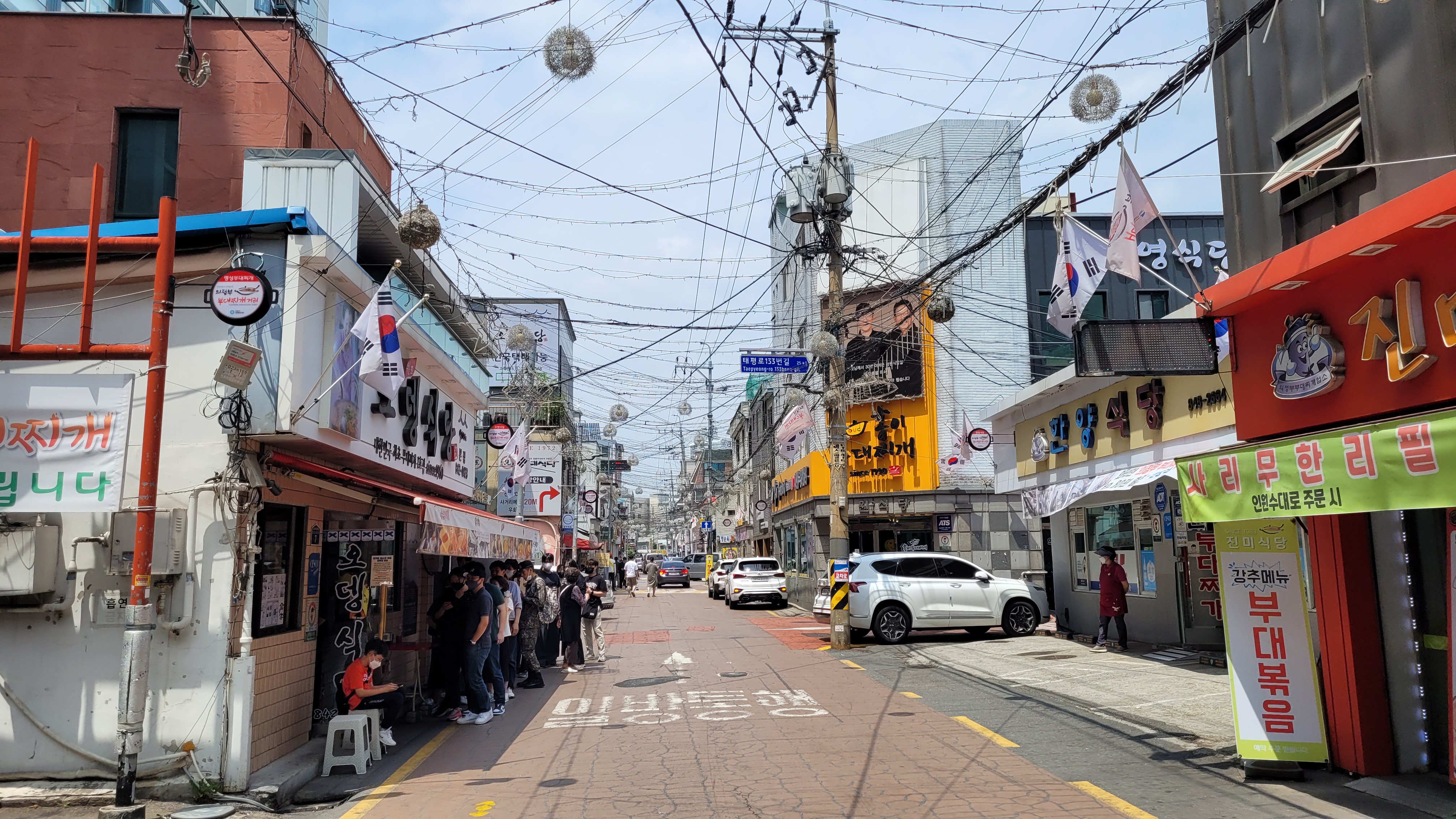 번화한 한국 거리, 복잡한 전선, 상점 간판, 식당 대기줄, 차량