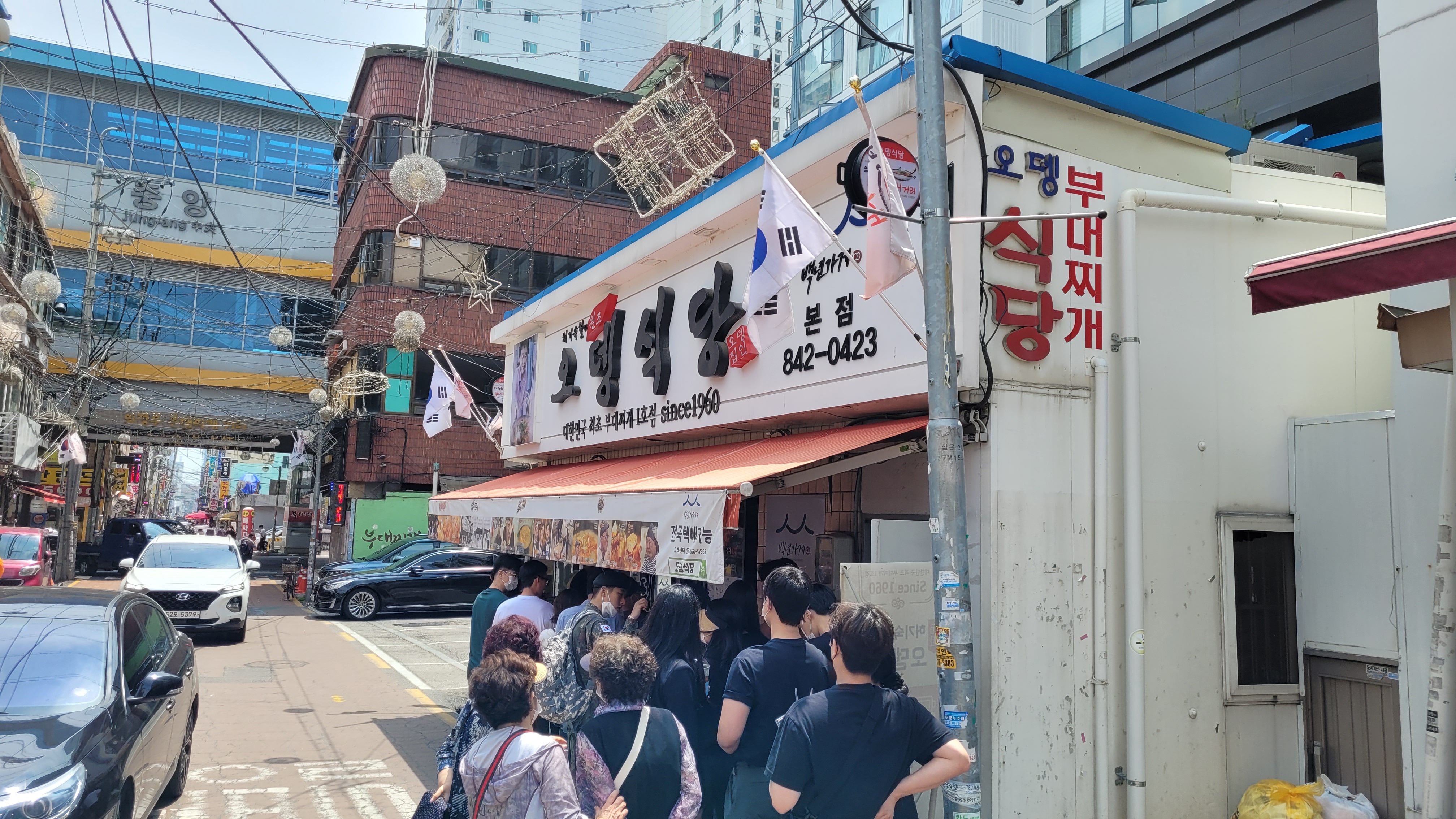 번화가 오뎅식당 부대찌개 전문점 앞 대기열. 태극기 게양.