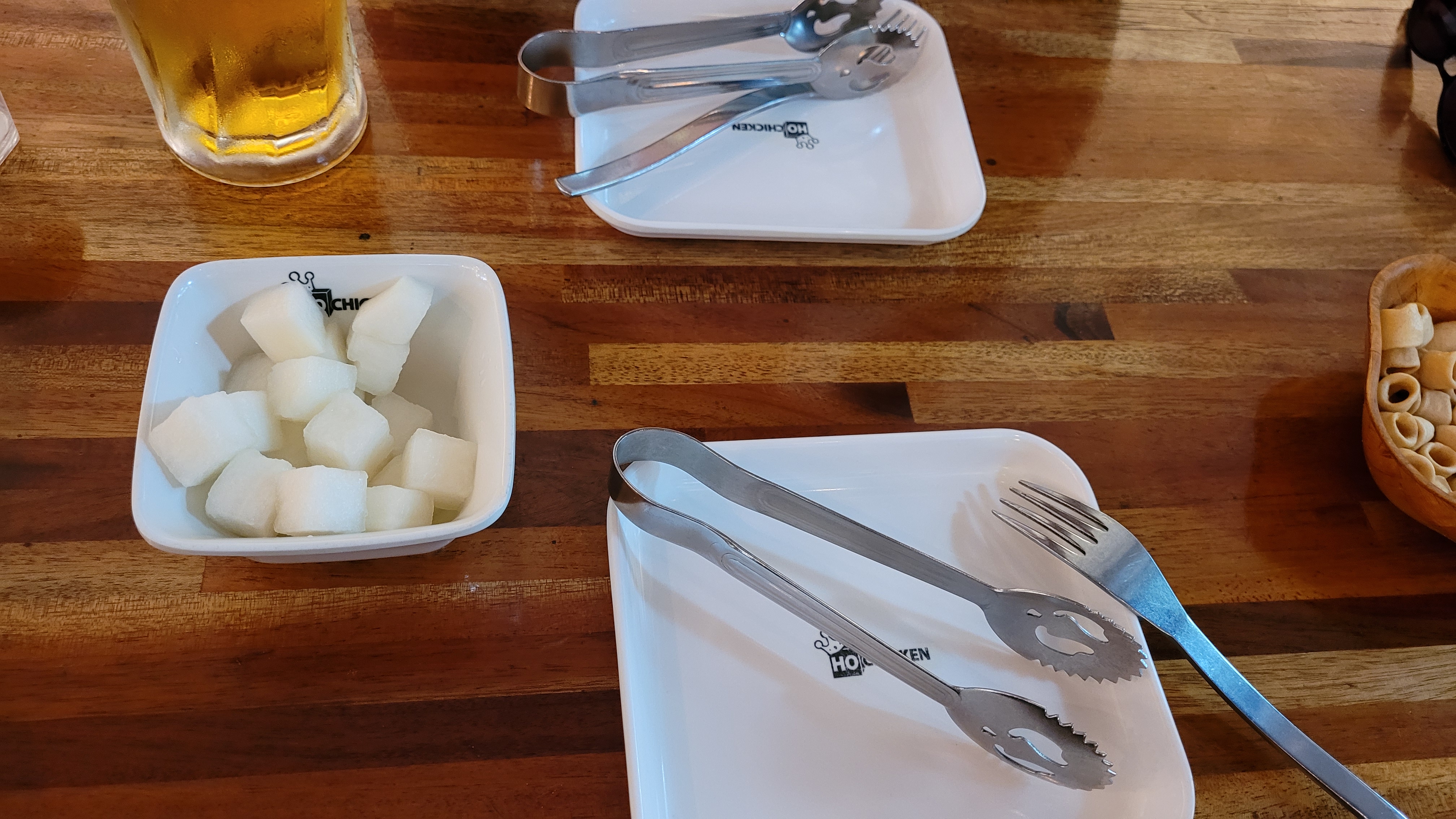 나무 식탁 위 시원한 맥주, 깍두기, 치킨 집게 포크.