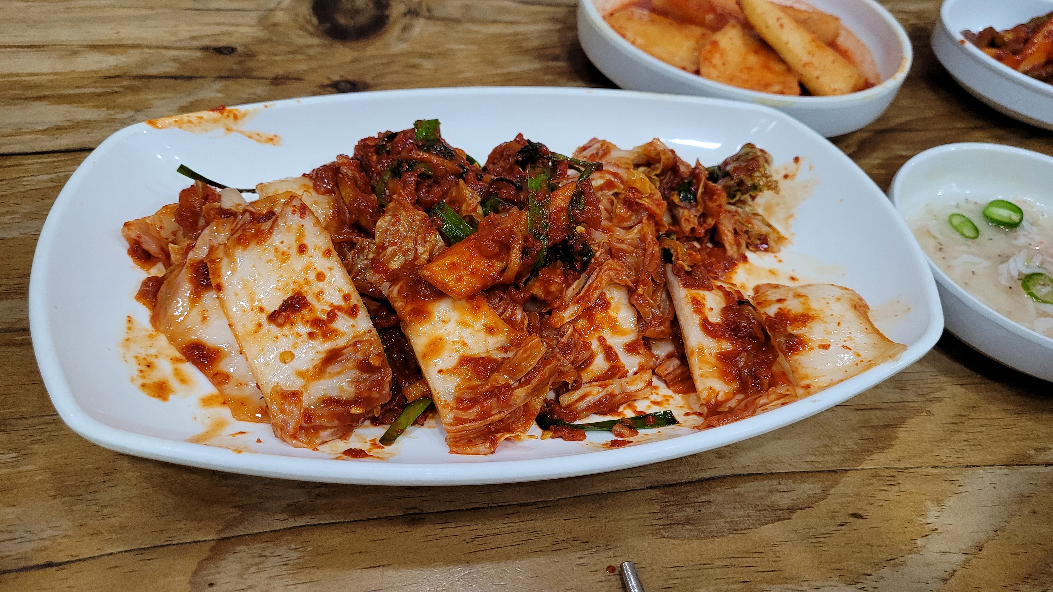 빨간 양념 썰린 배추김치, 하얀 접시에 담긴 밑반찬