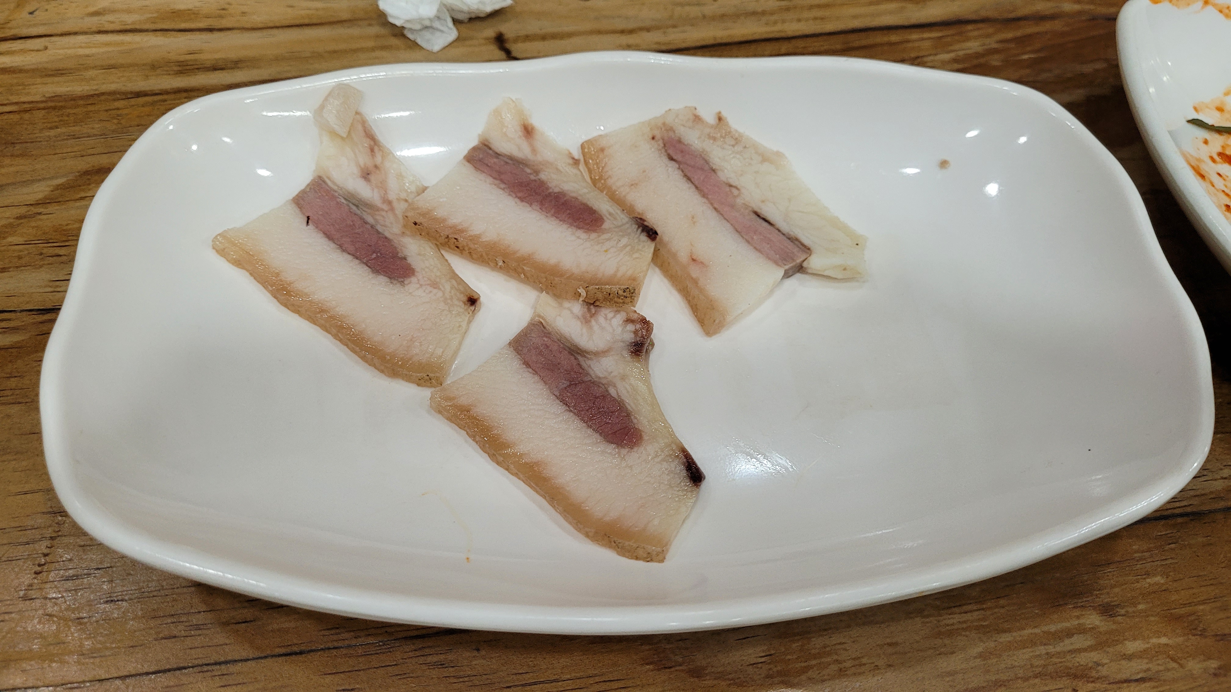 네 조각 돼지고기 수육, 지방 살코기 층, 흰 접시, 나무 식탁.