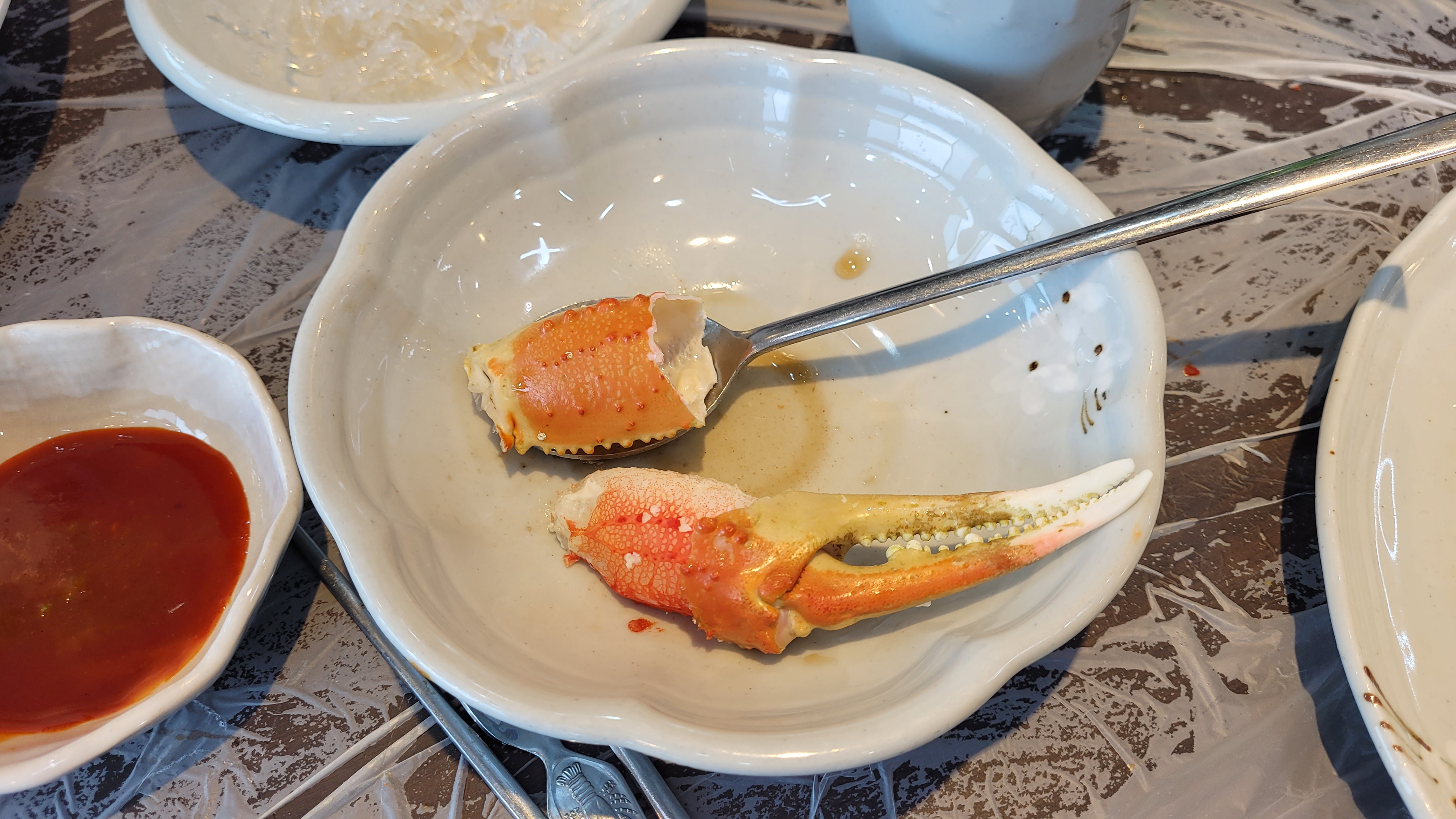 흰 접시 위 게살, 게 집게발, 숟가락, 빨간 소스