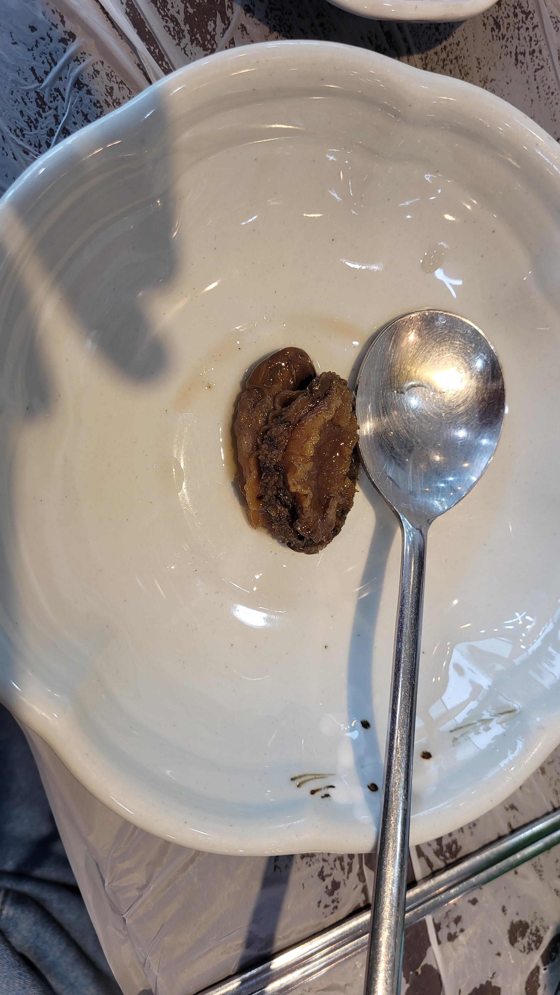 흰 도자기 그릇에 담긴 갈색 조리 전복과 은색 숟가락