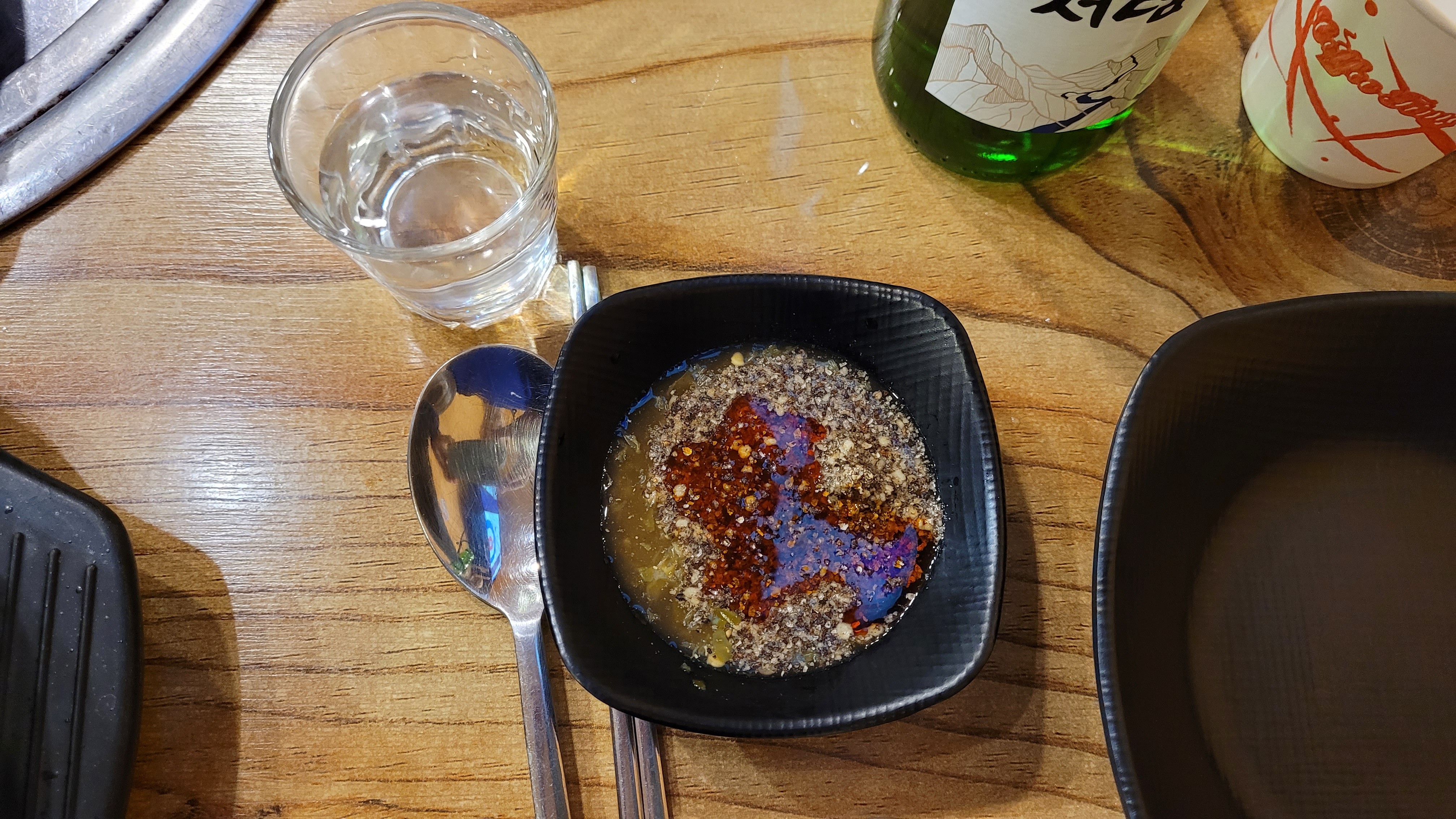 고춧가루 깨 기름장, 소주병, 물컵, 숟가락, 나무 식탁