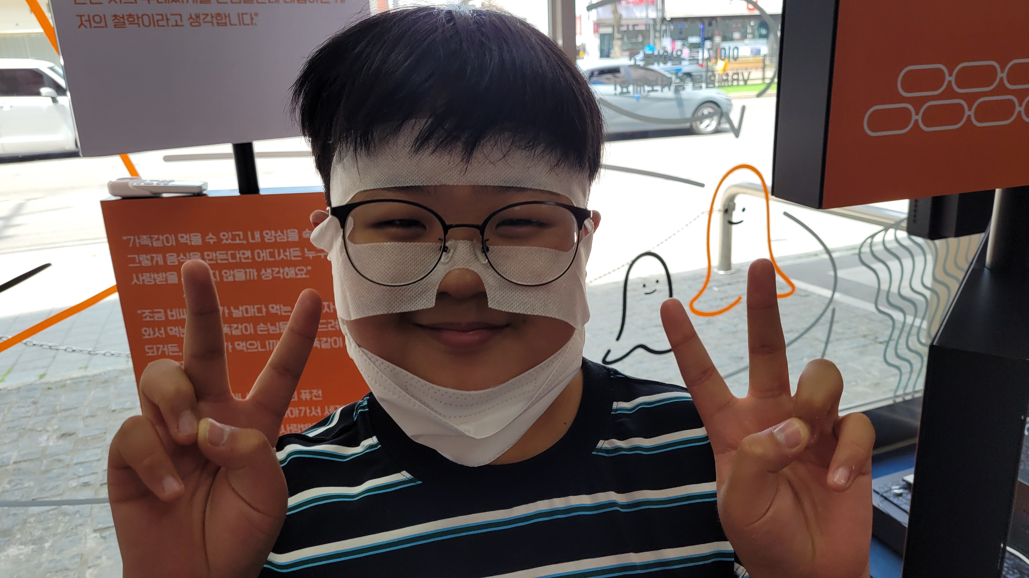 안경 쓴 밝은 아이, 얼굴 밴드와 마스크, 양손 브이 표시