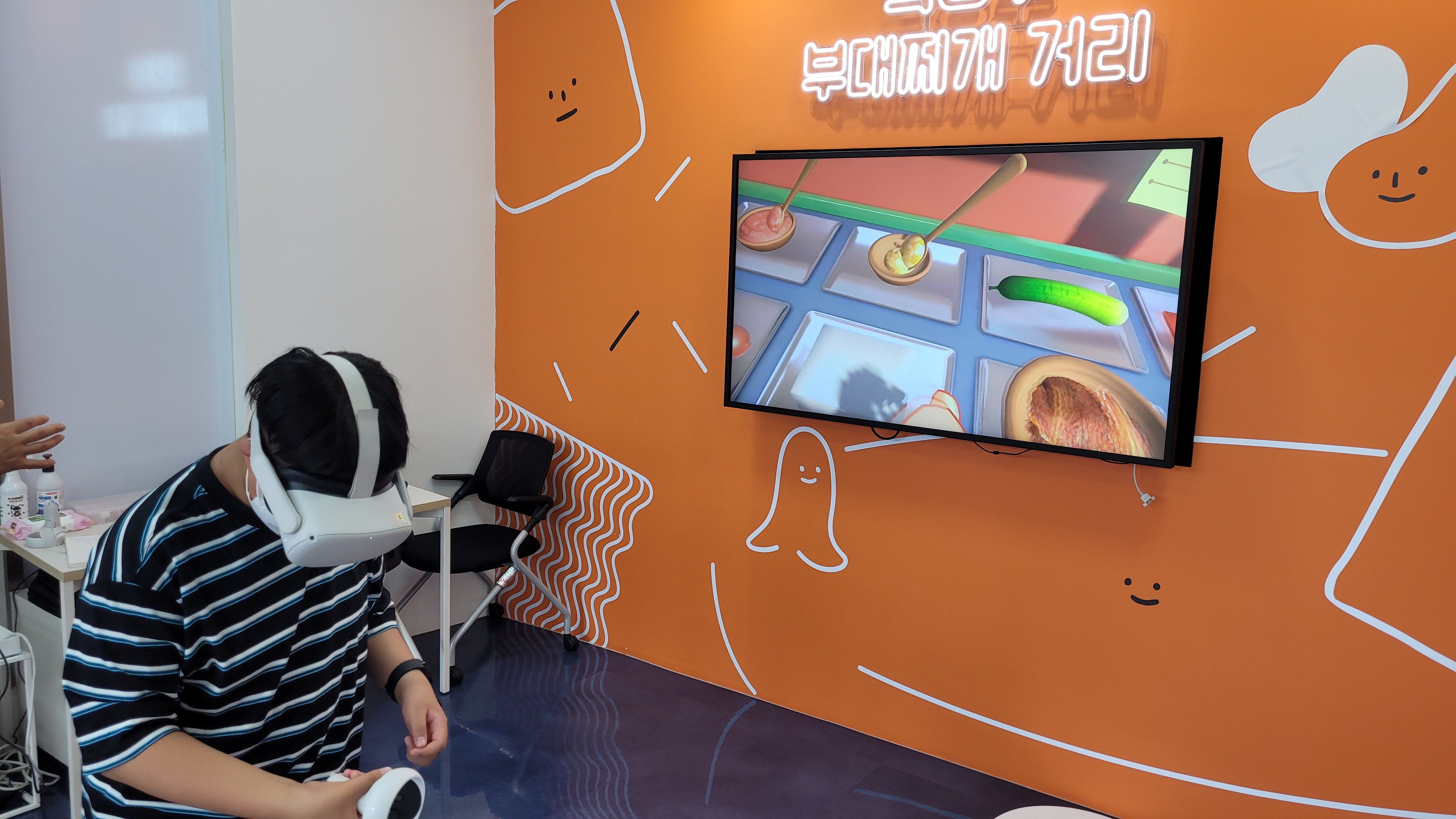 VR 헤드셋 착용 게임 체험, 오렌지 벽면 부대찌개 거리.