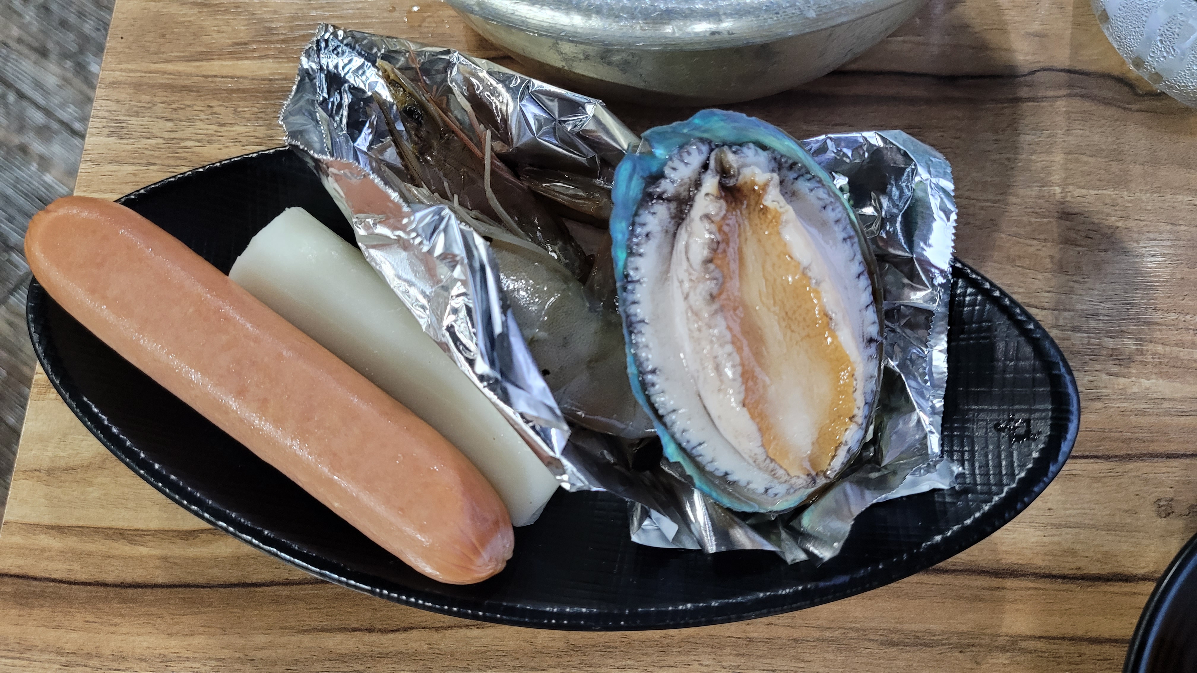 소시지, 떡, 은박지 새우, 전복 담긴 검은 접시