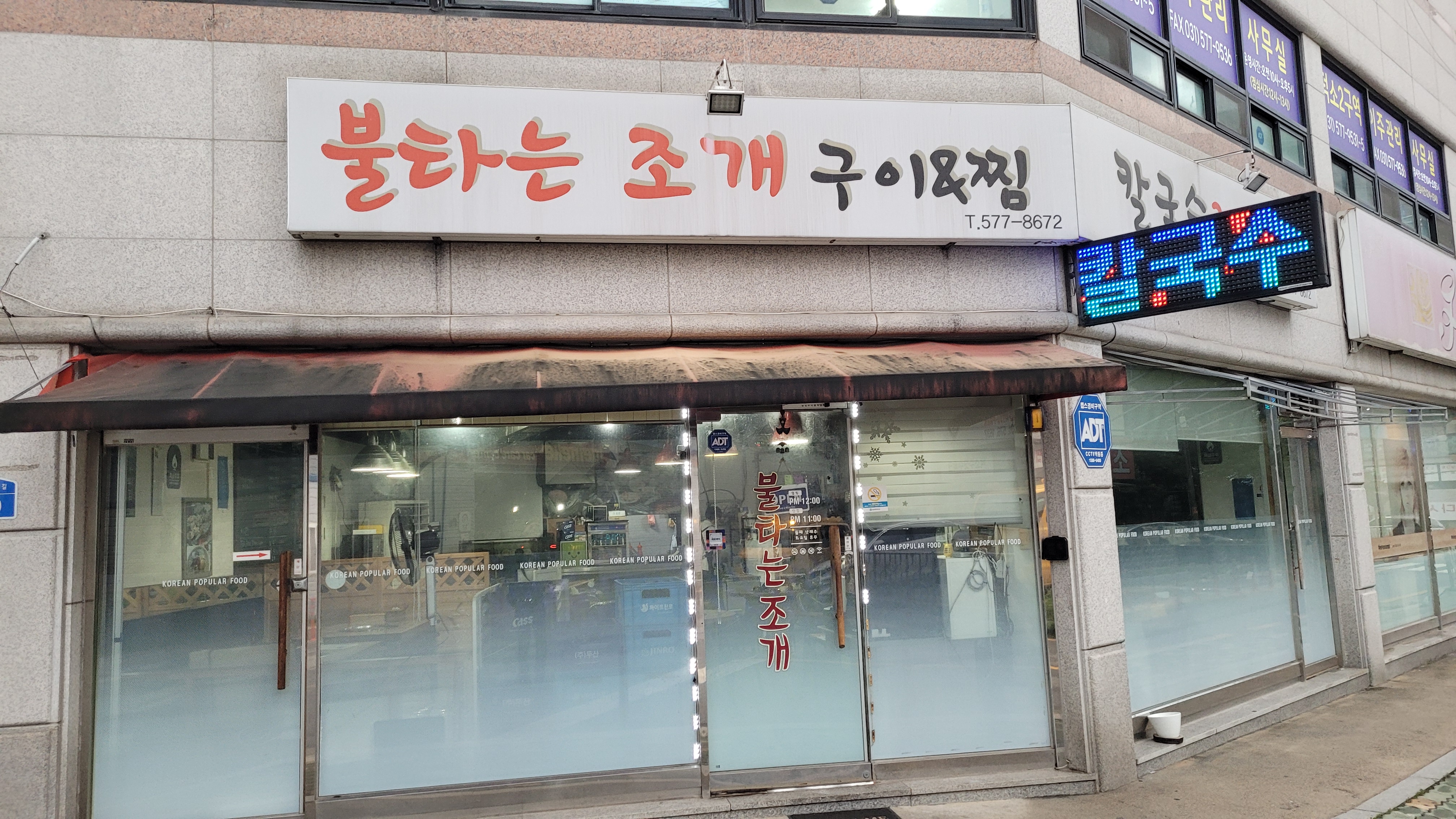 도시 코너 건물, 불타는 조개 구이 간판, 이발소 폴, 비 젖은 도로