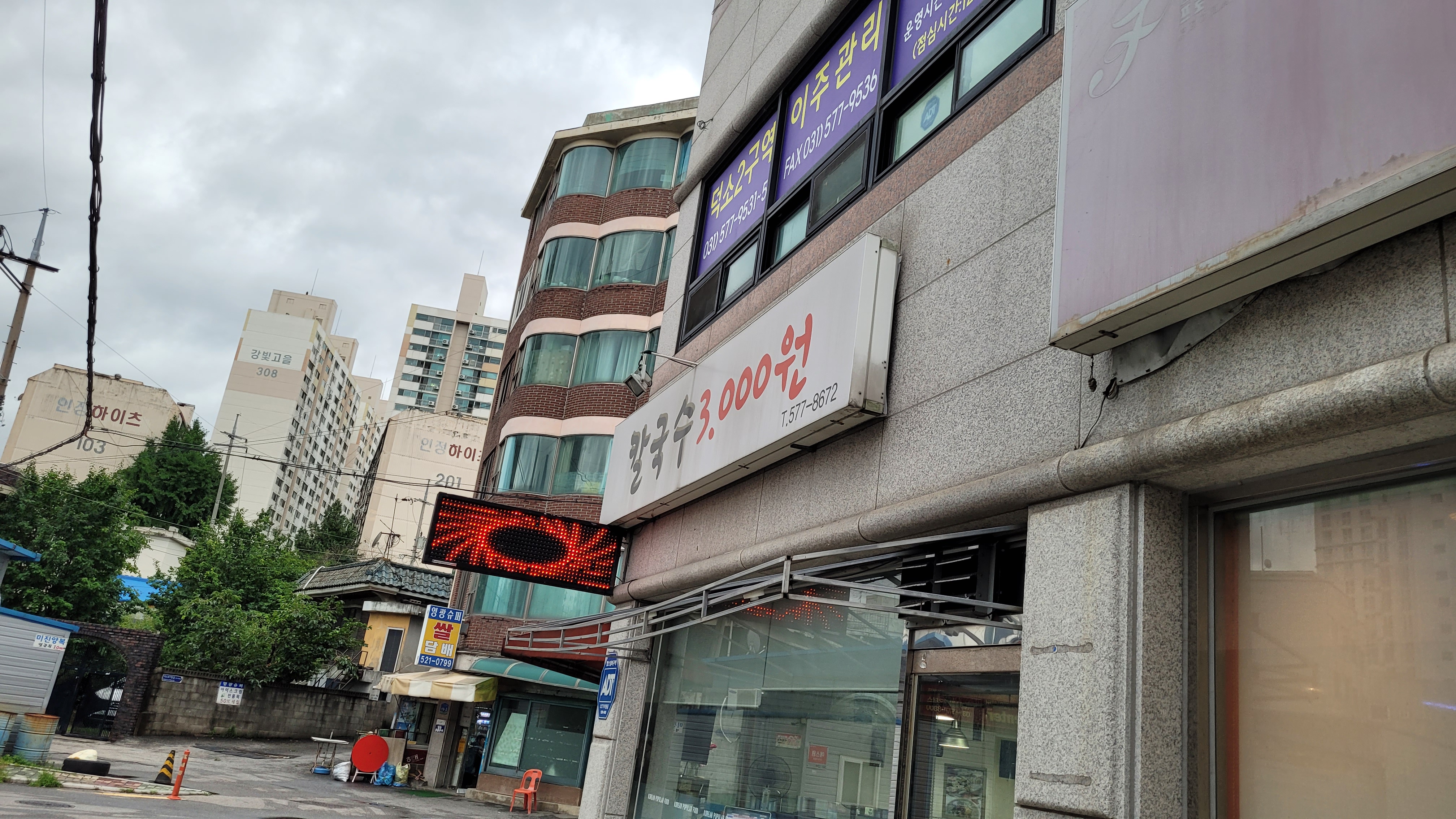 흐린 하늘 아래 도시 거리, 칼국수 3천원 간판과 붉은 LED