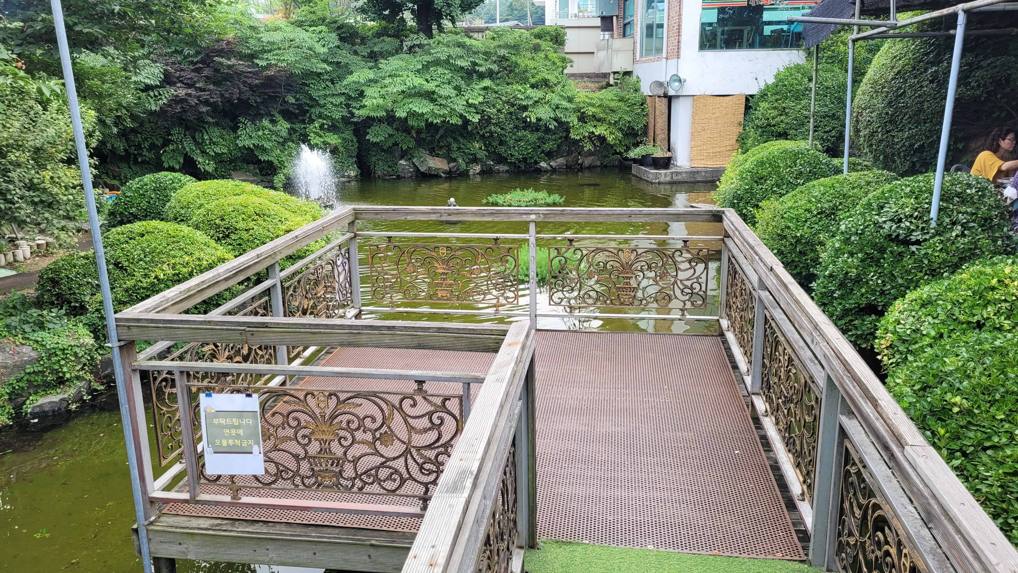 연못 분수, 울창한 숲 배경 금속 장식 난간 데크