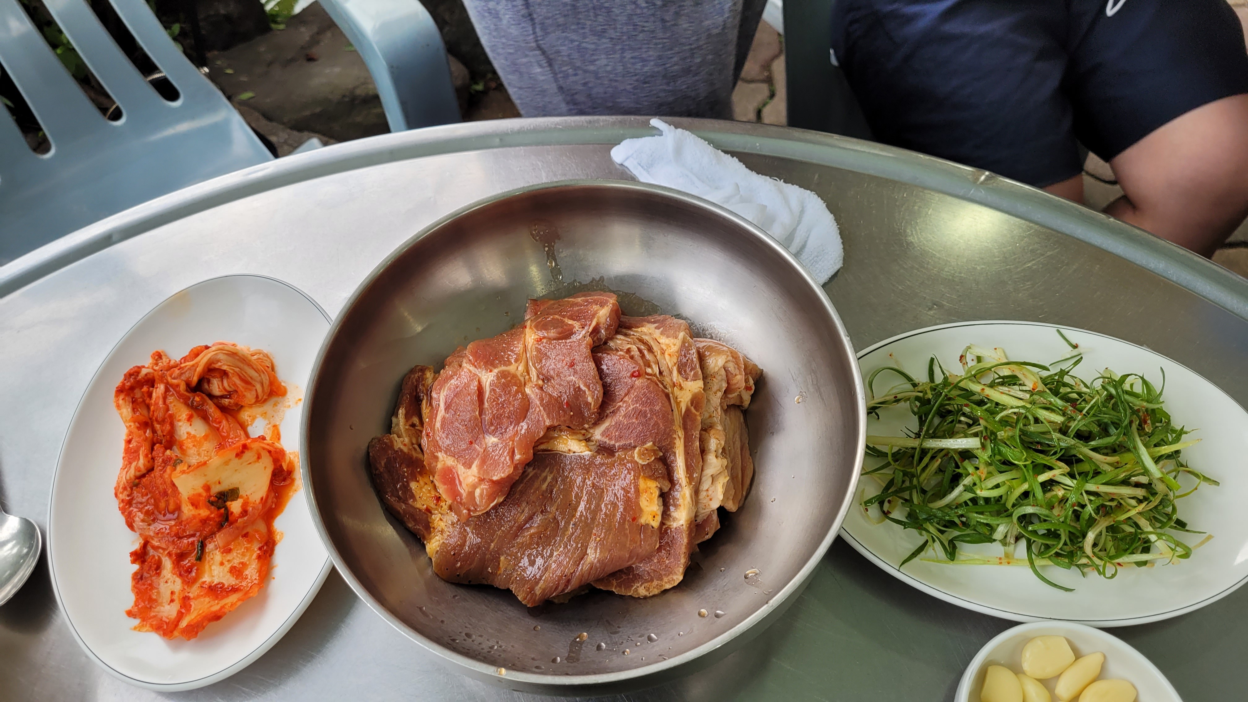 구이용 양념 돼지고기, 김치, 파채, 마늘 곁들인 한식 상차림.