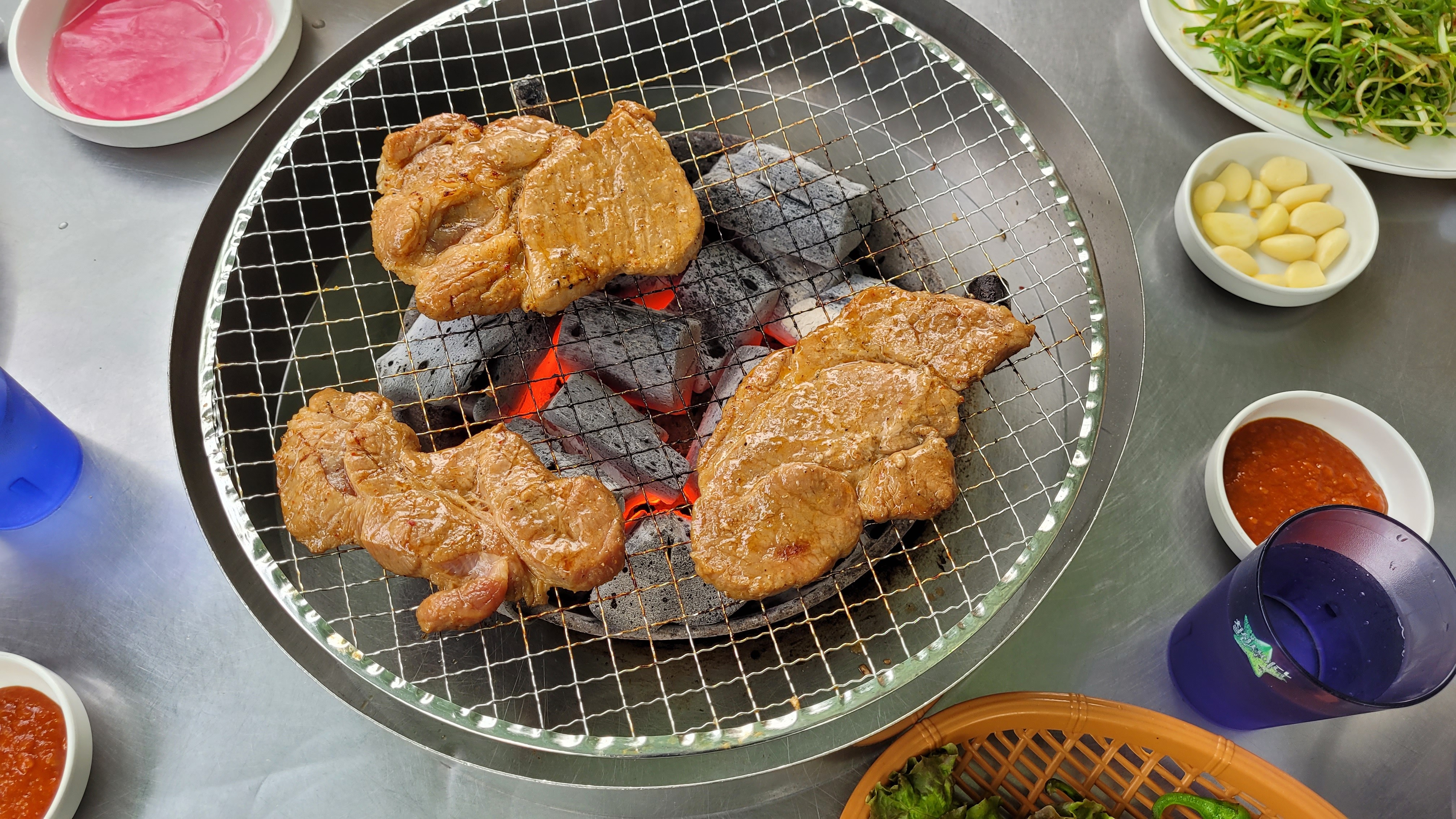 뜨거운 숯불 석쇠 위 양념 고기 구이, 마늘, 파무침, 쌈채소