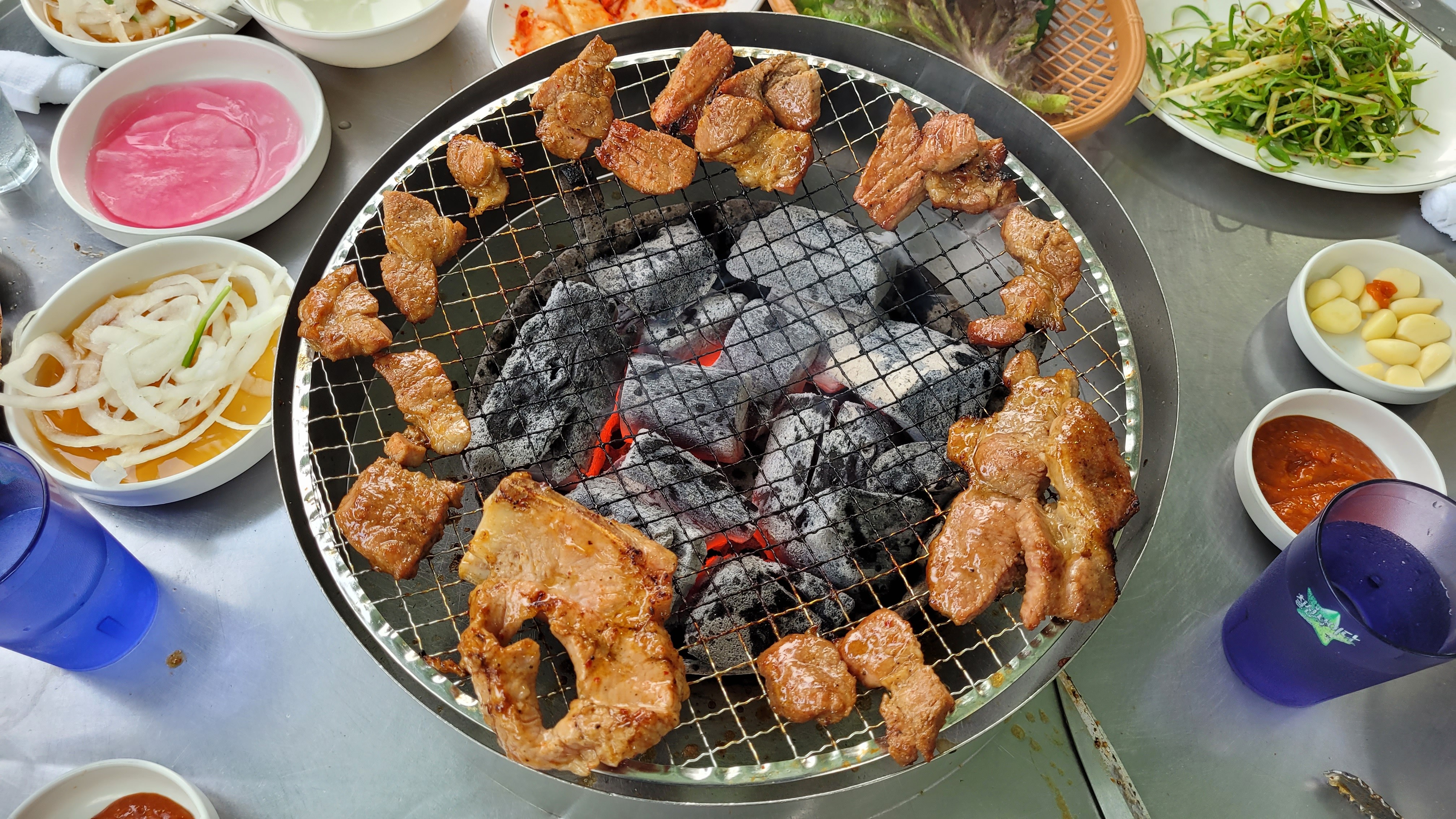 뜨거운 숯불에 구워지는 돼지갈비, 식탁 위 반찬들