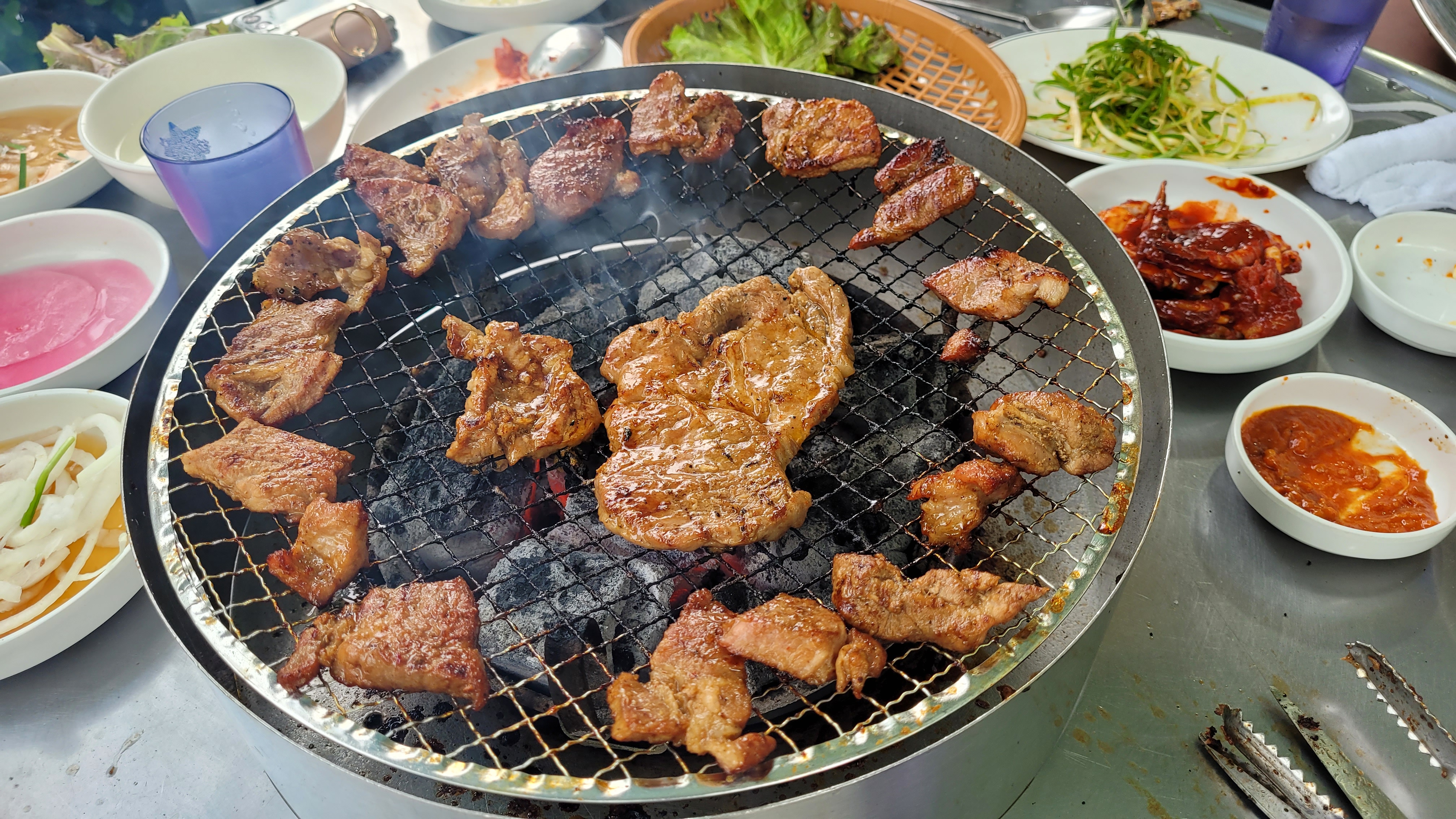 숯불 석쇠 위 맛있게 구워지는 돼지갈비, 연기, 반찬들