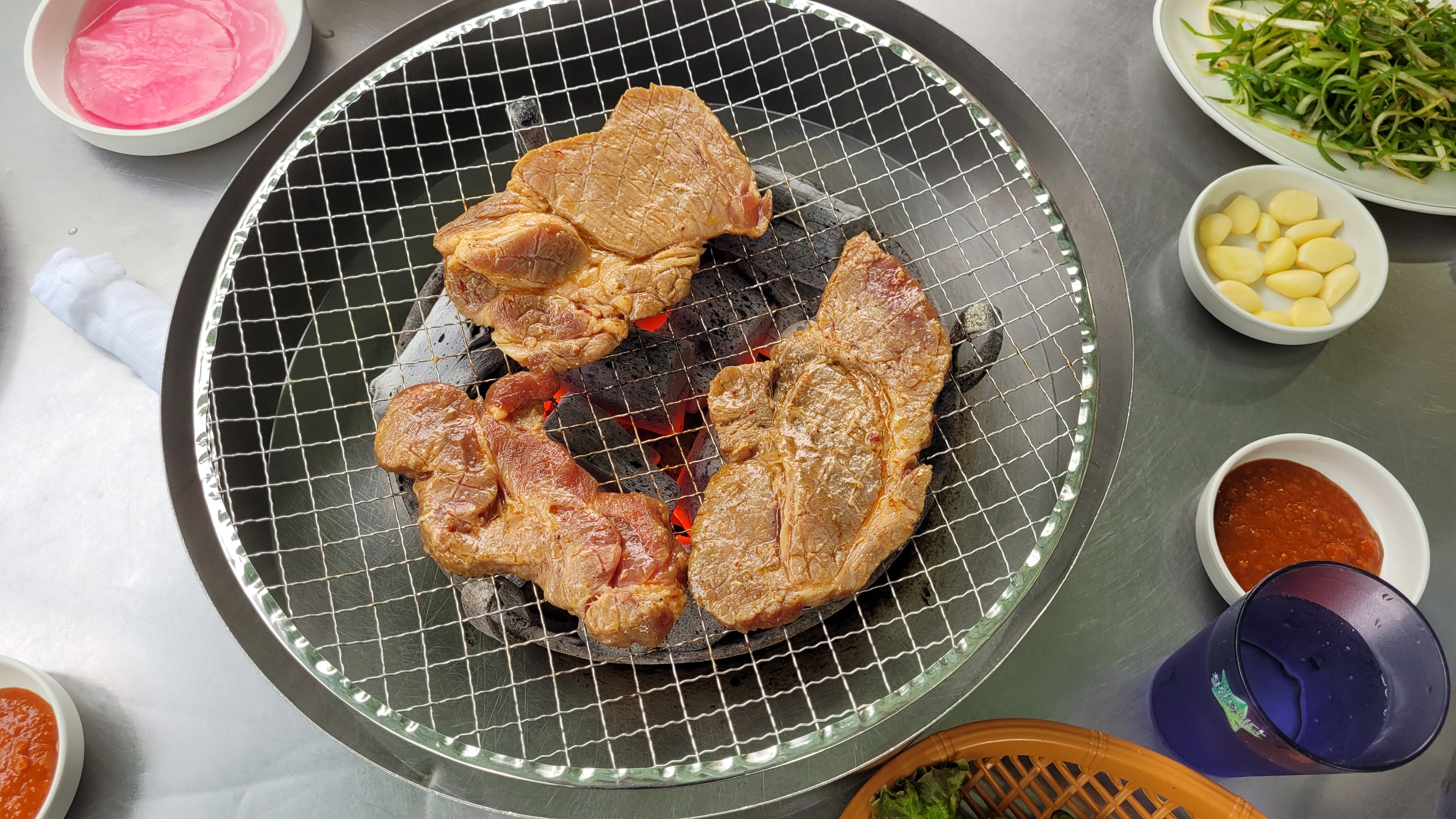 양념 돼지고기 숯불 석쇠 구이, 금속 테이블 위 여러 한식 반찬