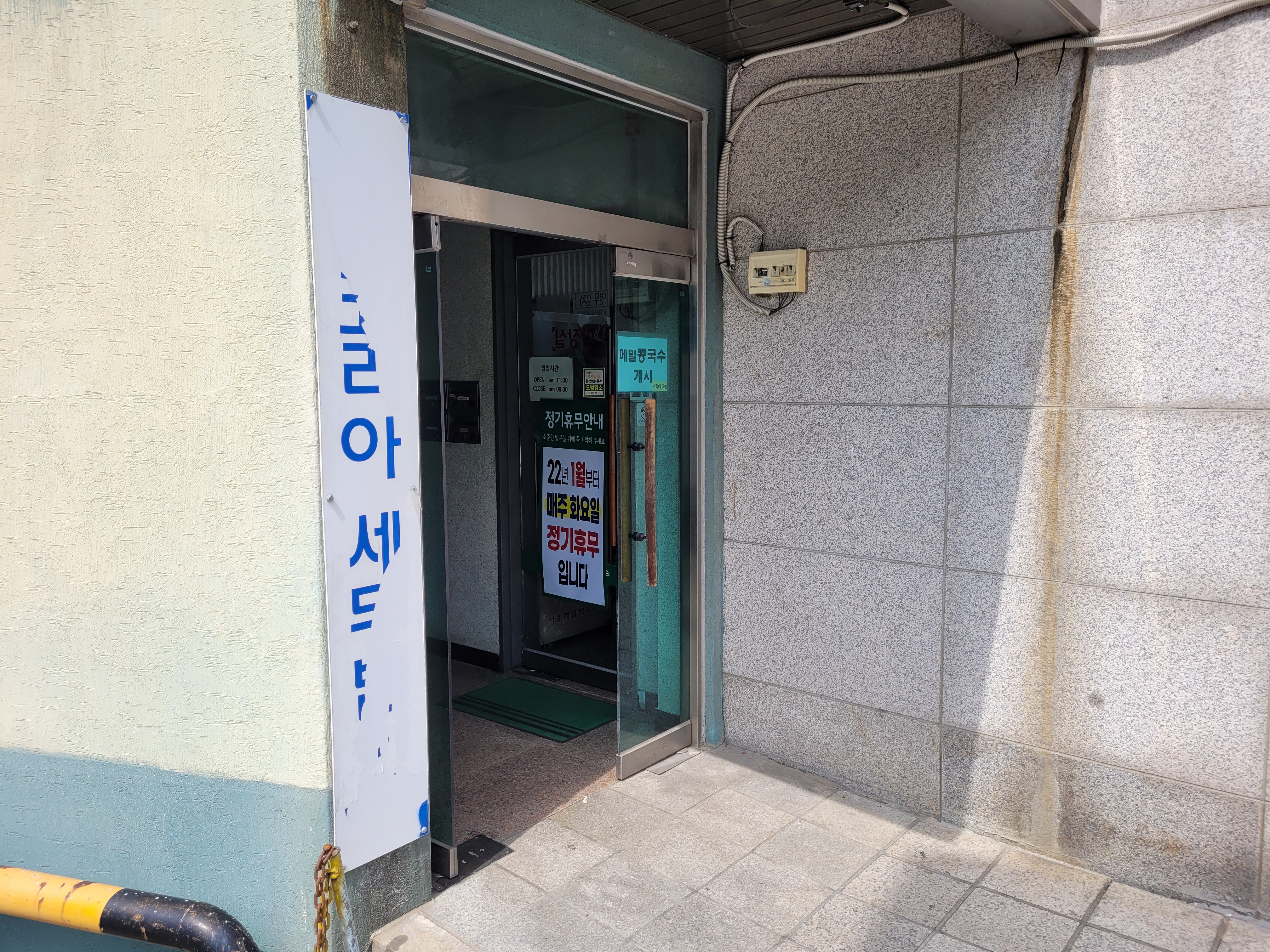 건물 출입구 유리문, 메밀콩국수 간판, 정기휴무 안내, 타일 벽