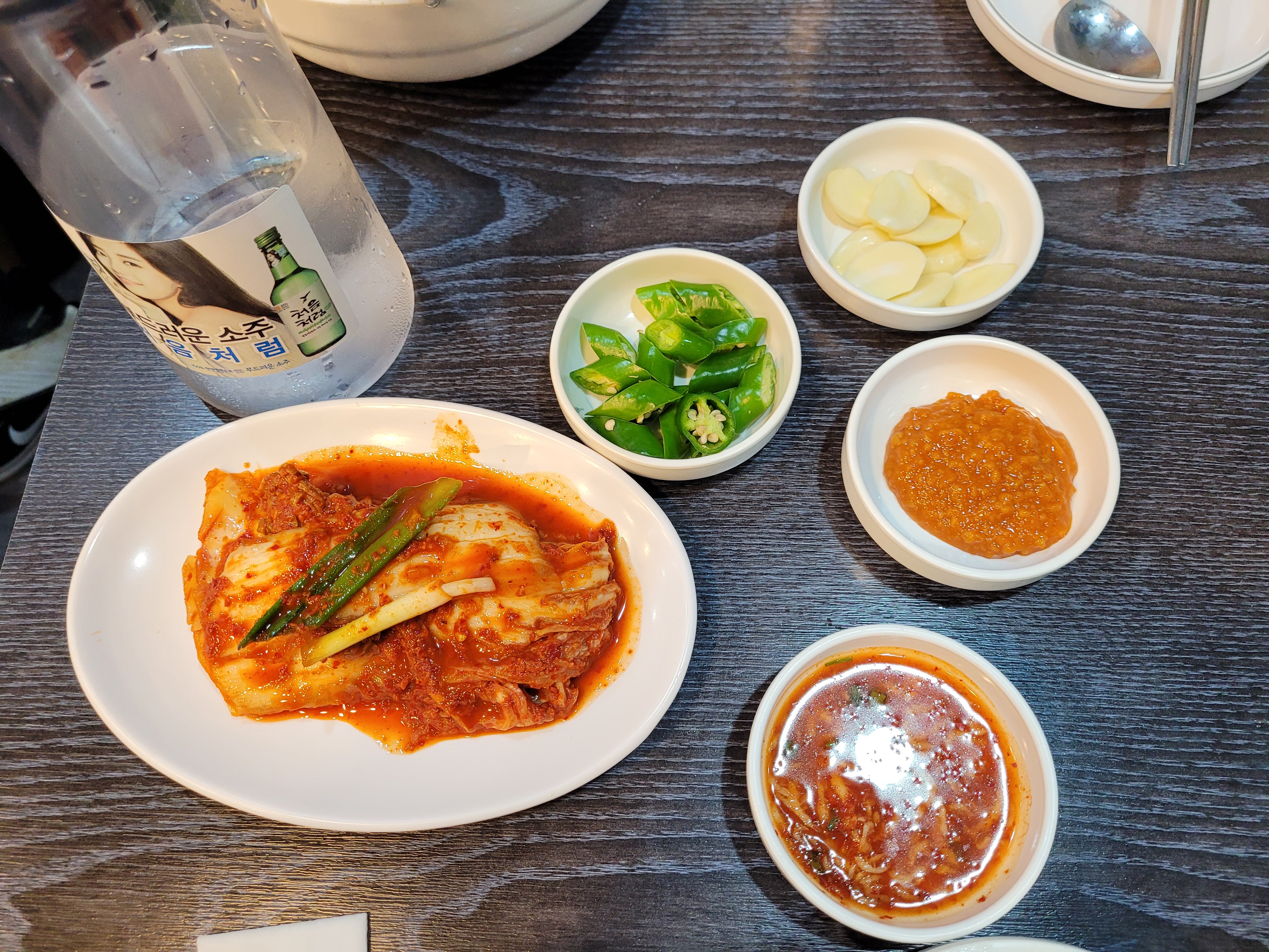 소주 병, 김치, 풋고추, 마늘, 쌈장, 어두운 테이블
