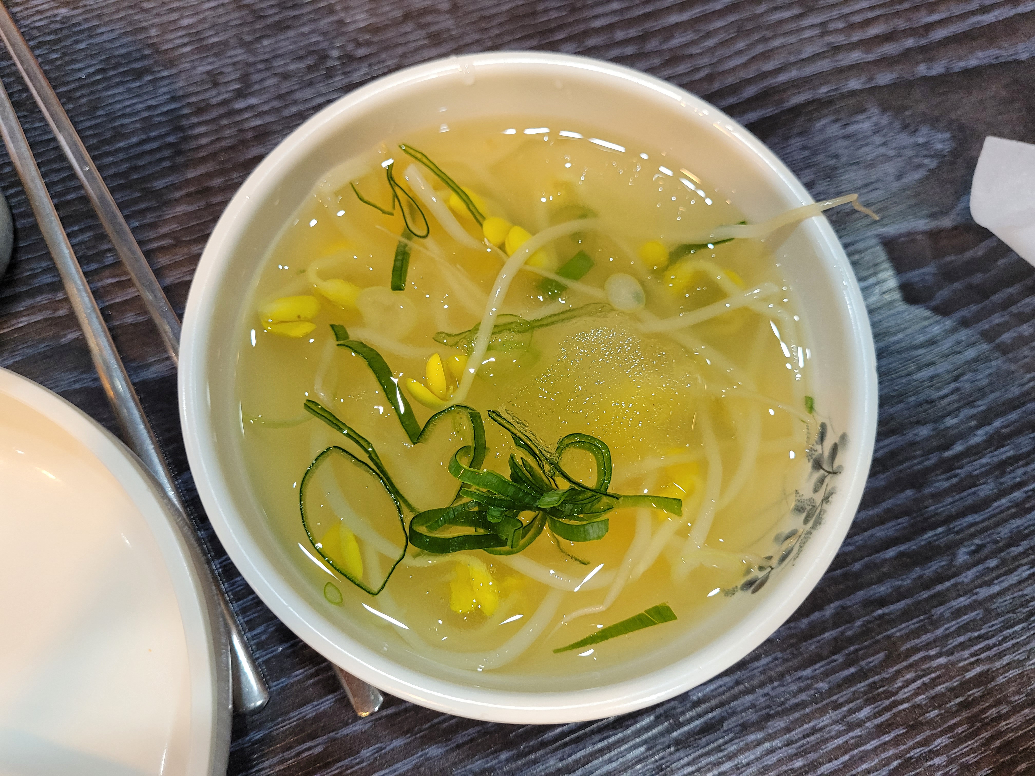 나무 탁자 위 흰 그릇, 맑은 콩나물국, 노란 콩나물, 파 고명
