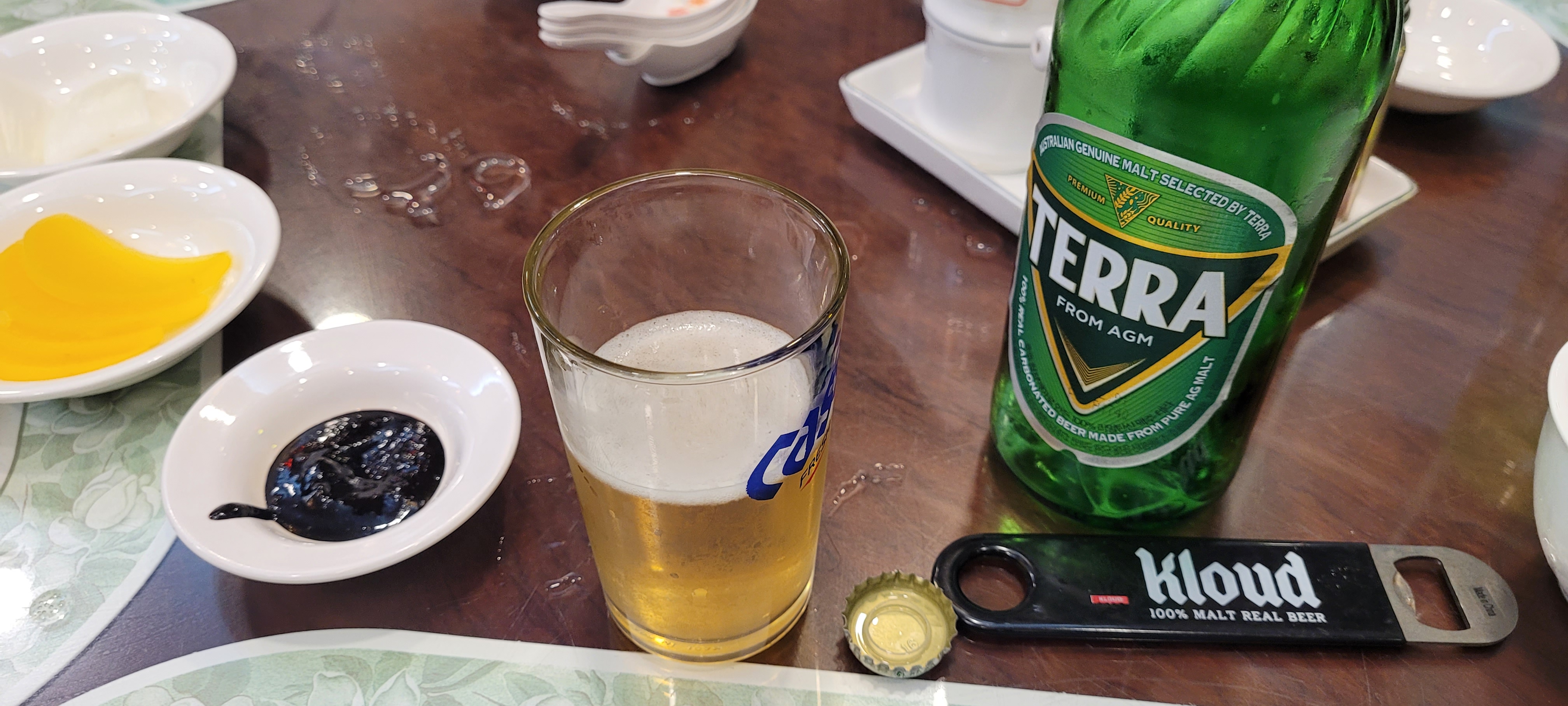 테라 맥주 병, 맥주잔, 클라우드 병따개, 단무지, 춘장 탁자.