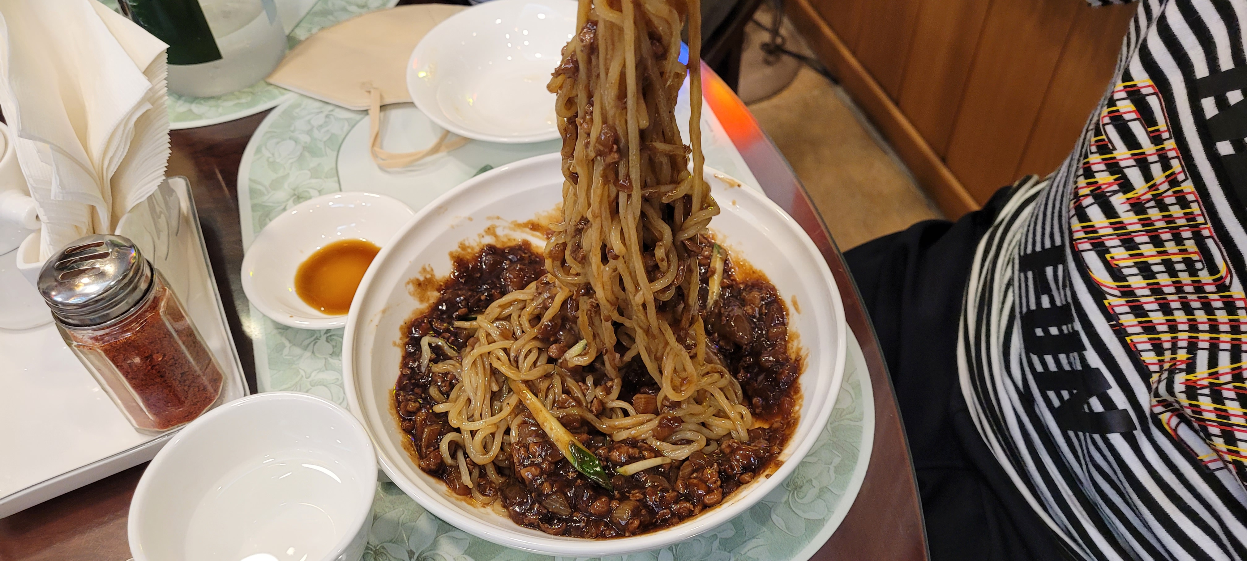 그릇에서 들어 올린 짜장면 면발, 윤기 나는 검은 소스 비빔.