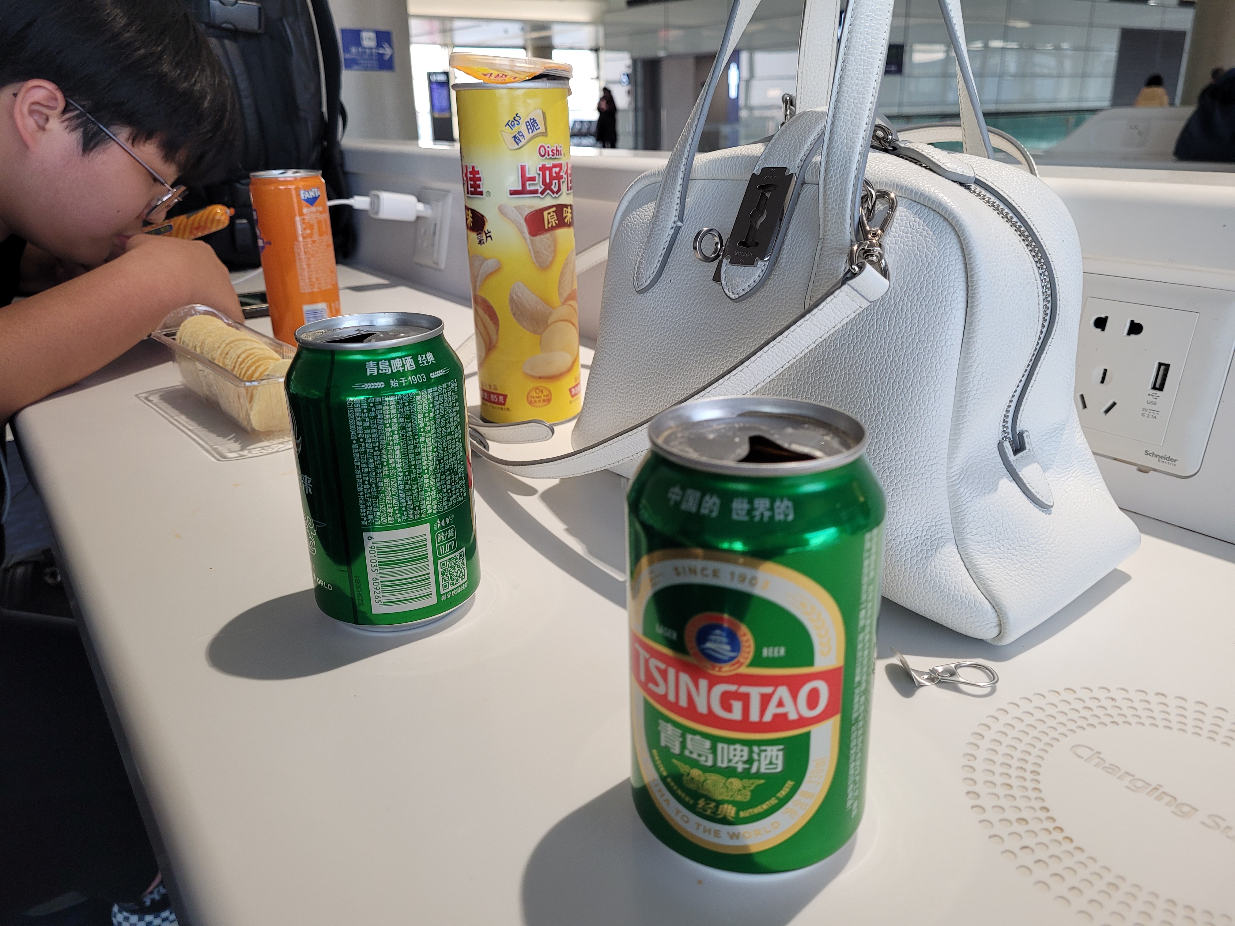 공항 테이블 위 칭따오 맥주캔들, 환타, 포테이토칩, 흰색 가방