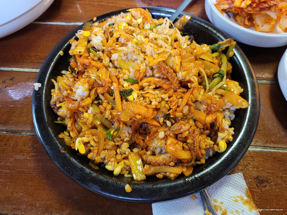 매콤한 낚지 볶음밥 검은 그릇 위 나무 식탁