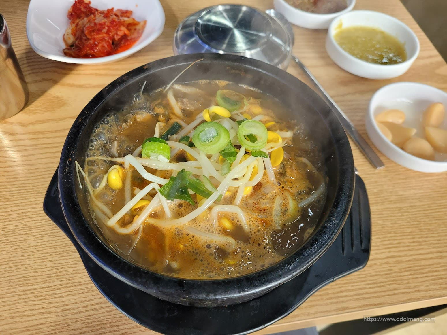 식탁 위 뜨거운 콩나물국밥, 파와 콩나물, 매콤한 김치 반찬.
