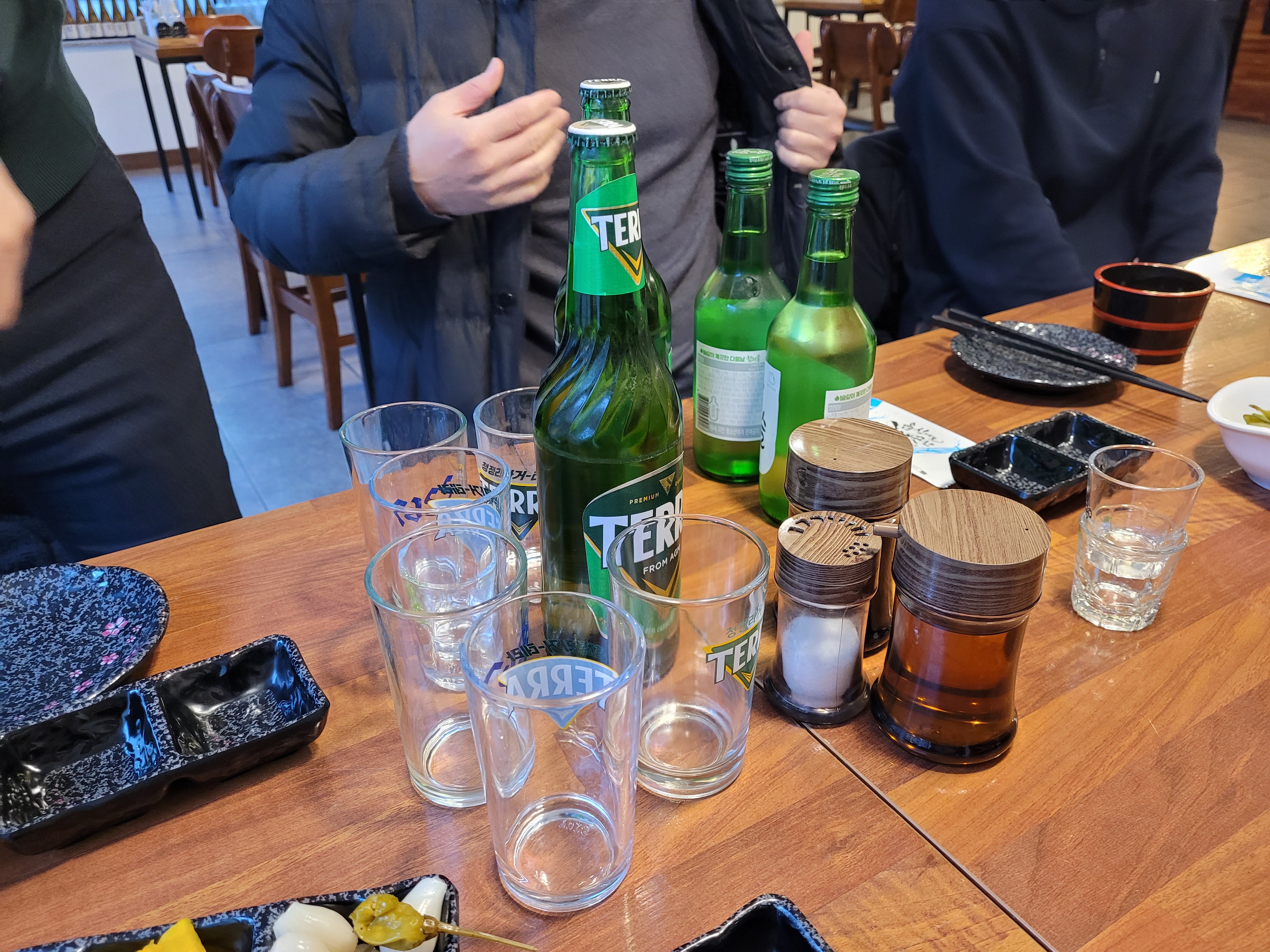 녹색 테라 맥주, 소주 병, 빈 잔, 식당 나무 탁자.