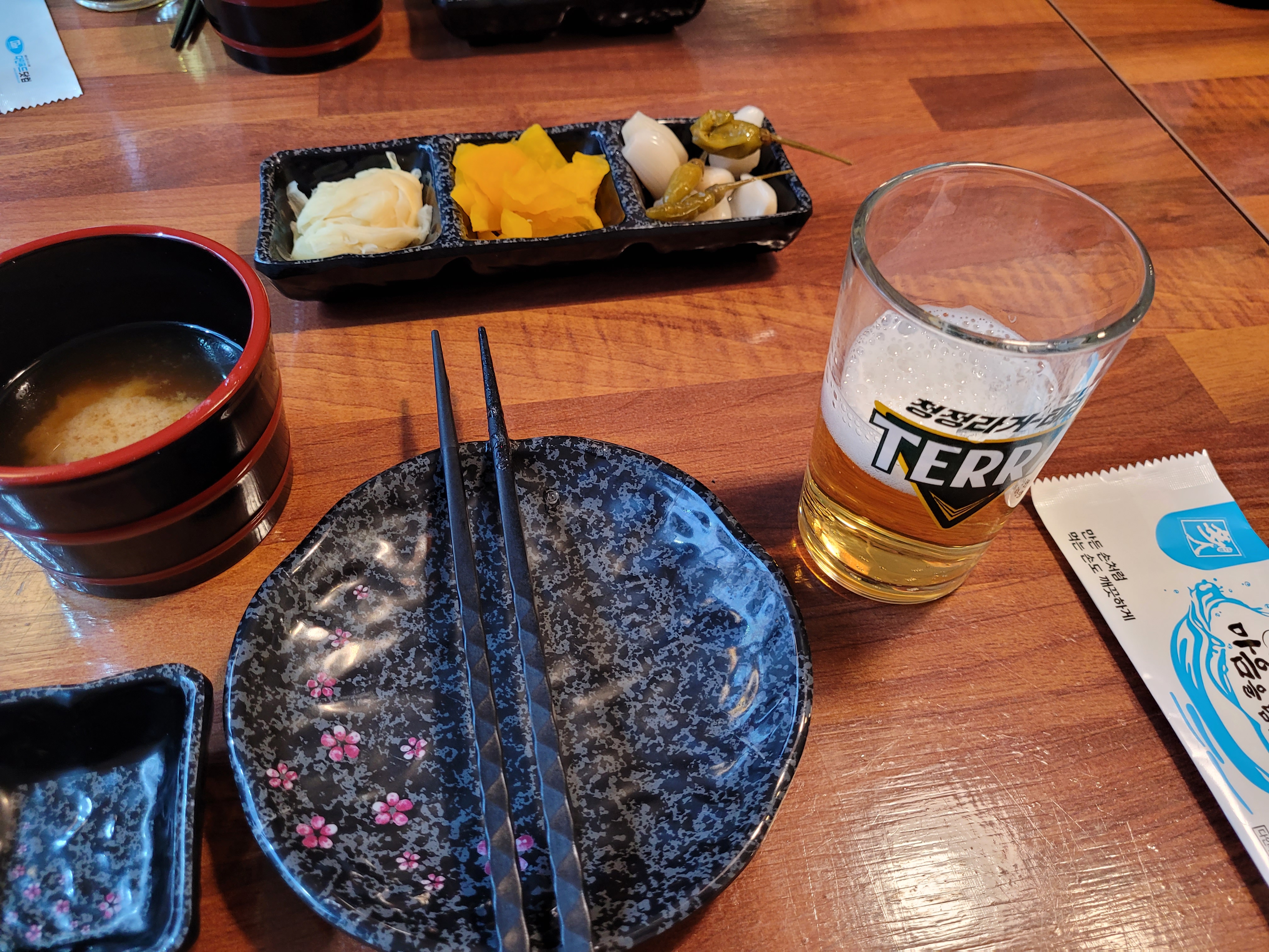 목조 탁자 위 맥주, 다양한 밑반찬, 젓가락, 따뜻한 국.